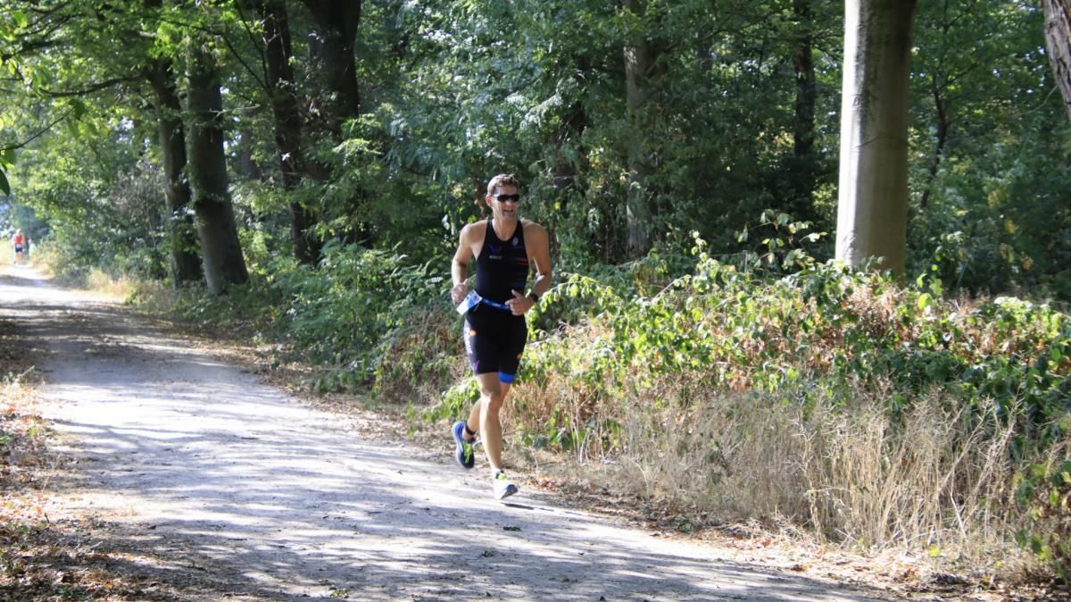 Een man rent over een zandpad in het bos.