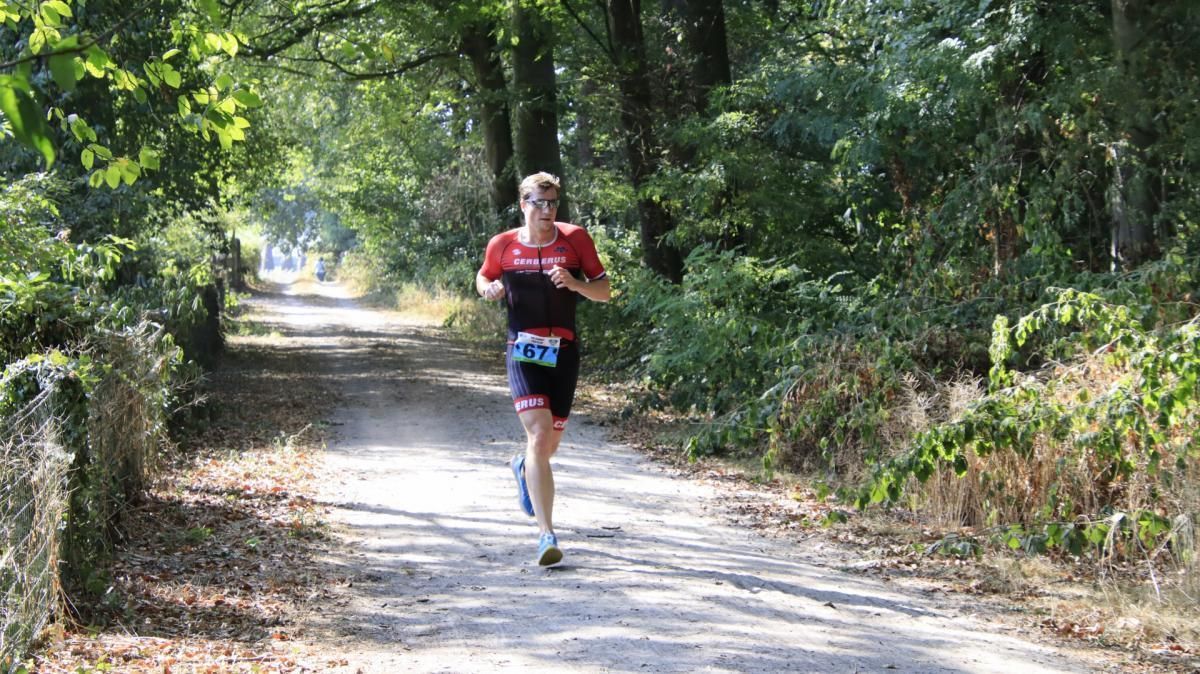 Een man rent over een onverharde weg in het bos.