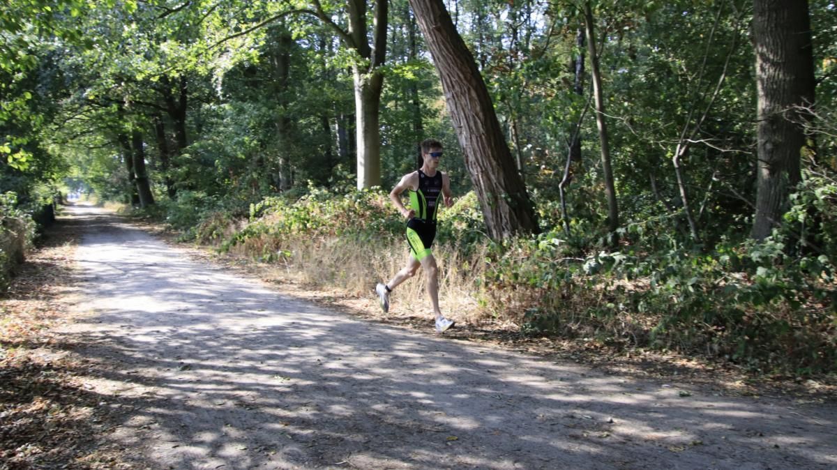 Een man rent over een onverharde weg in het bos.