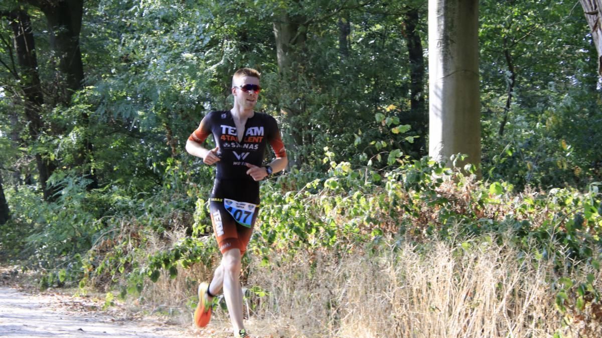 Een man rent over een onverharde weg in het bos.