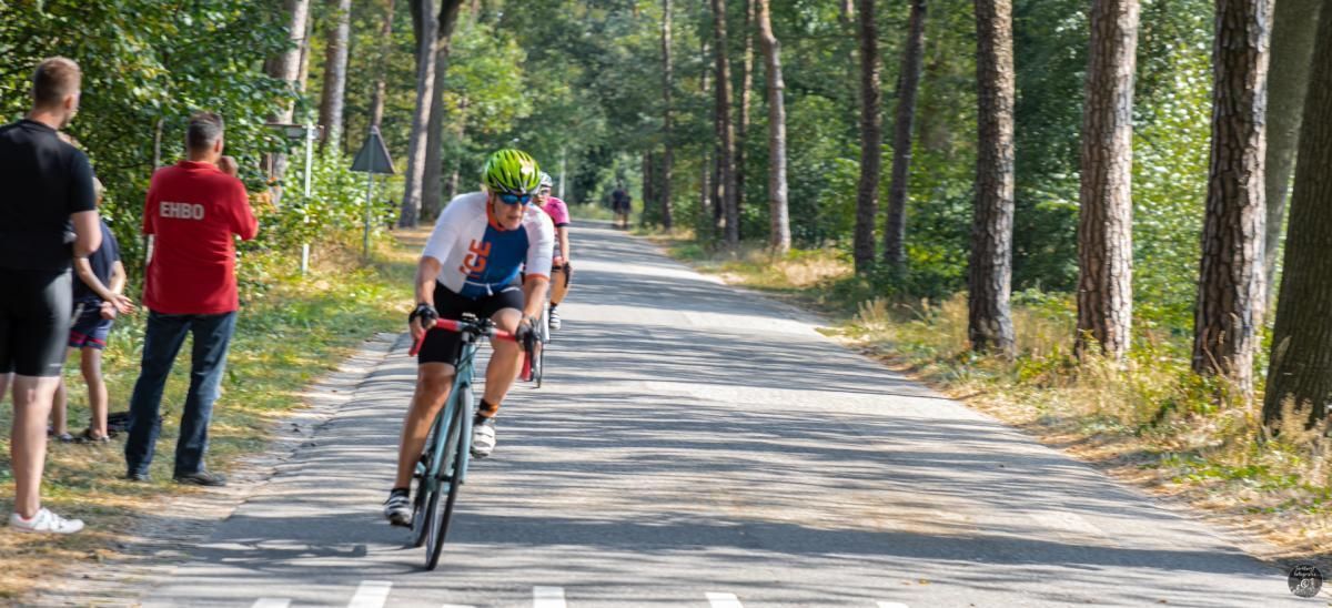 Een man fietst over een weg die omgeven is door bomen.