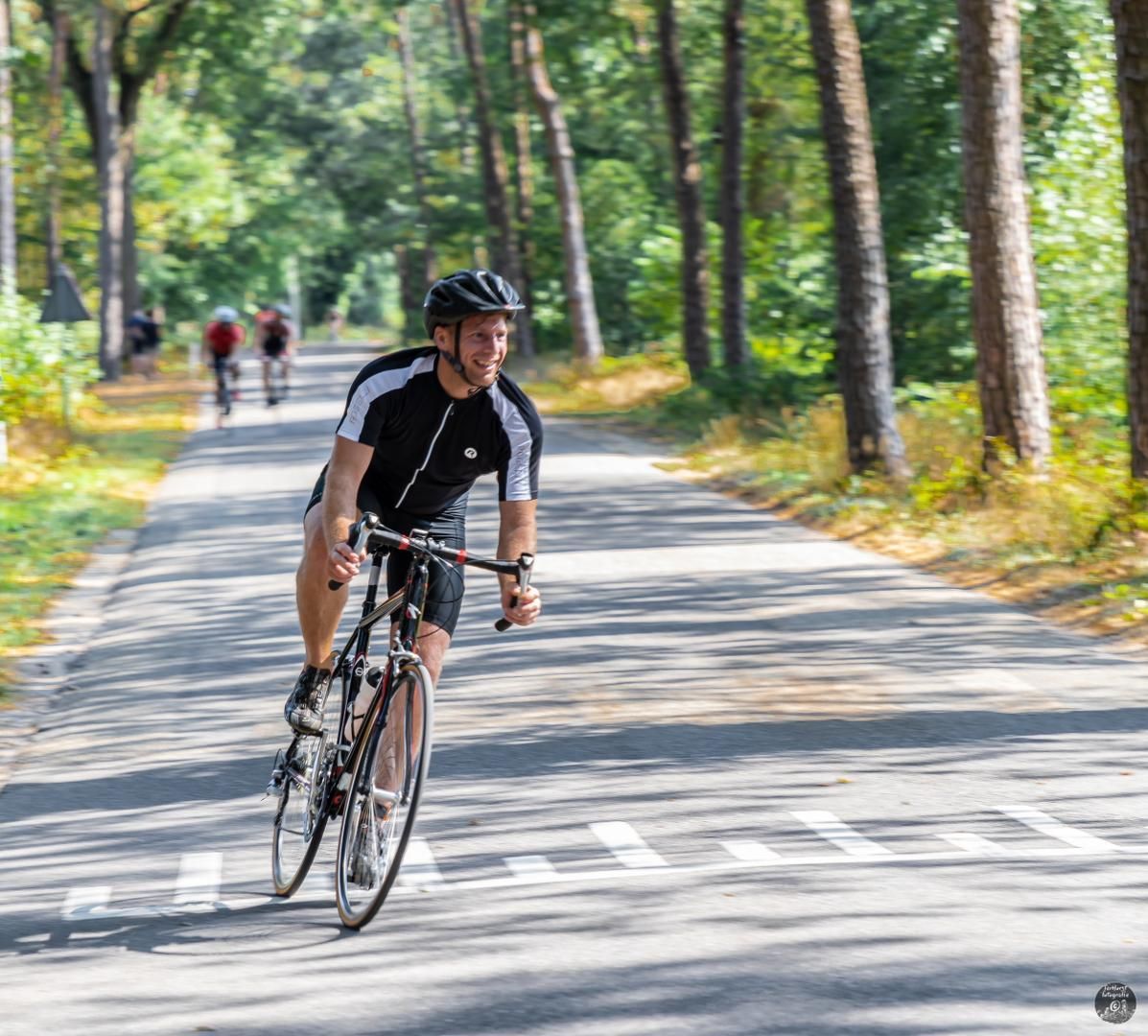 Een man met een helm rijdt op een fiets over de weg.