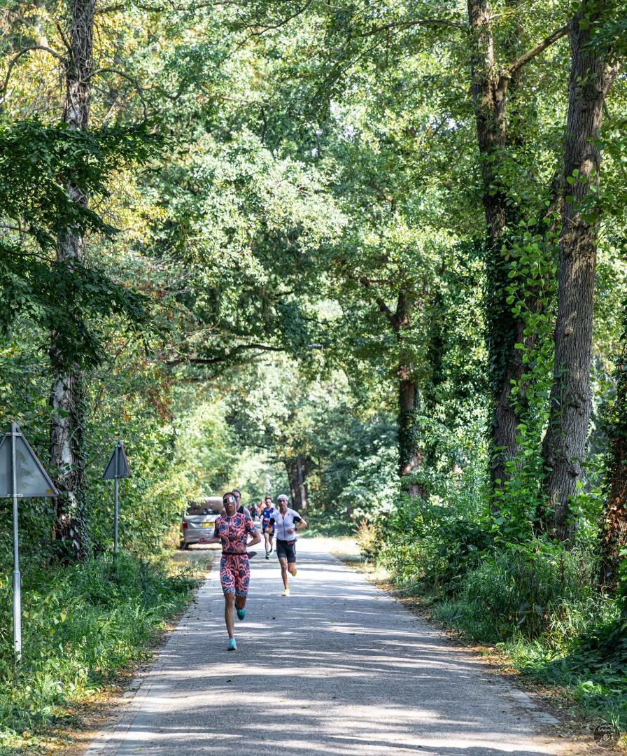 Een groep mensen rent over een onverharde weg, omringd door bomen.