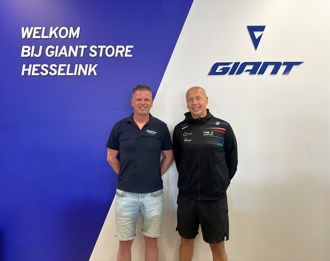 Twee mannen staan naast elkaar voor een groot winkelbord.