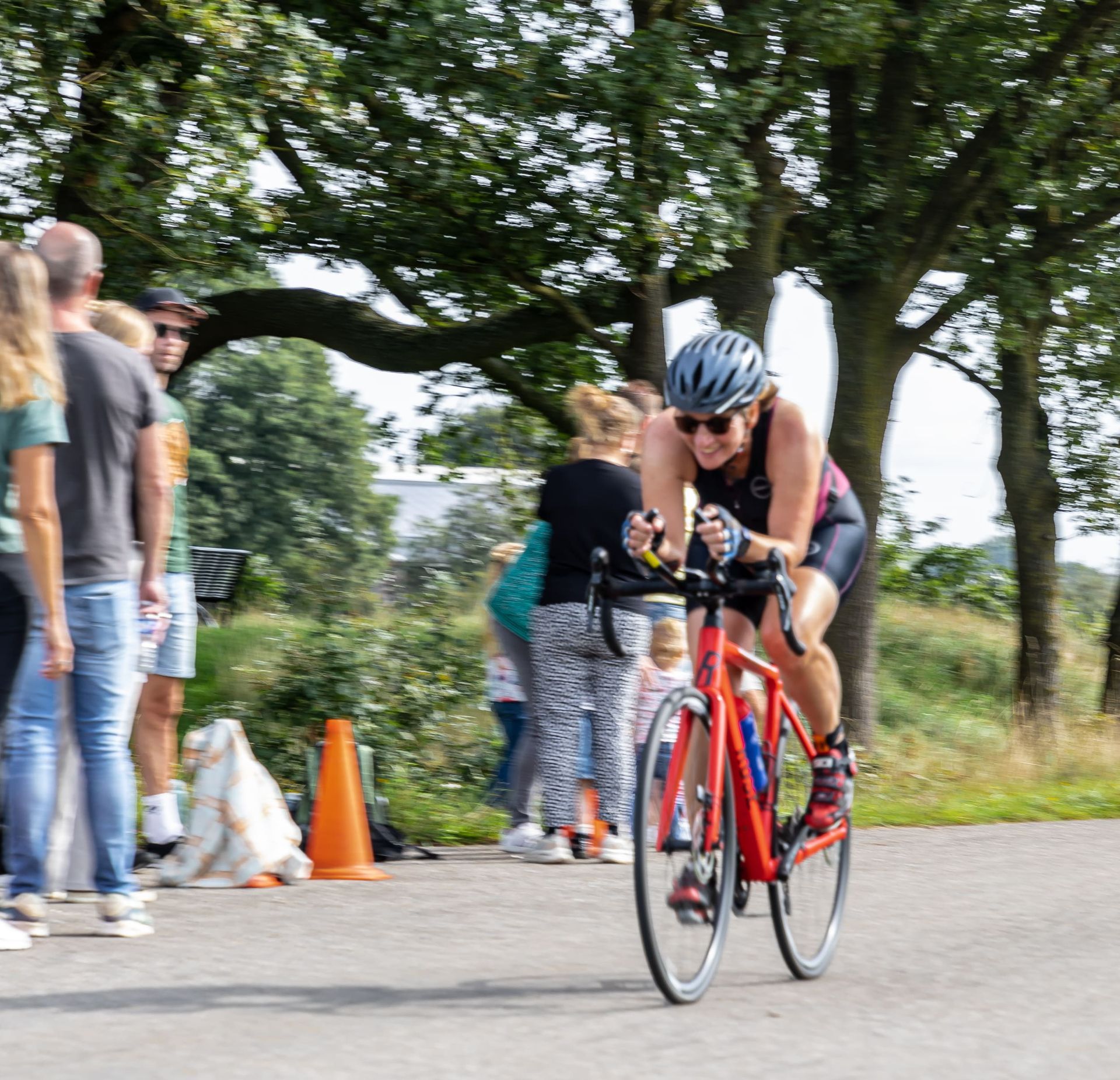 Een vrouw met een helm rijdt op een rode fiets over een weg