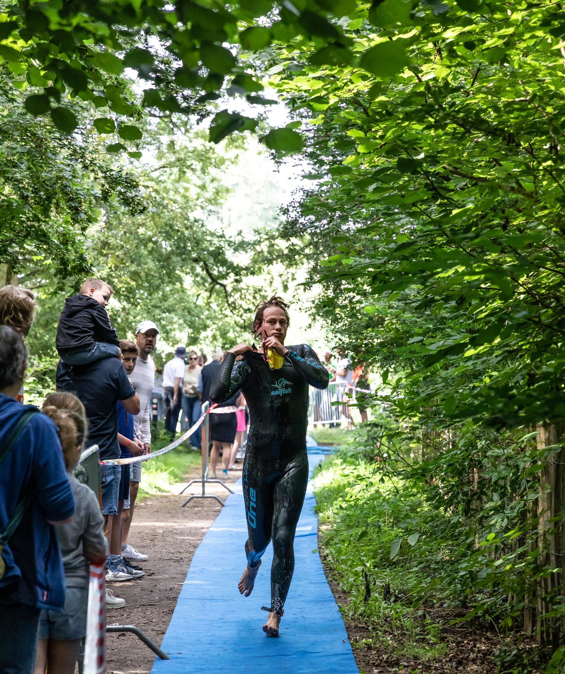 Een man in een wetsuit rent over een pad in het bos.