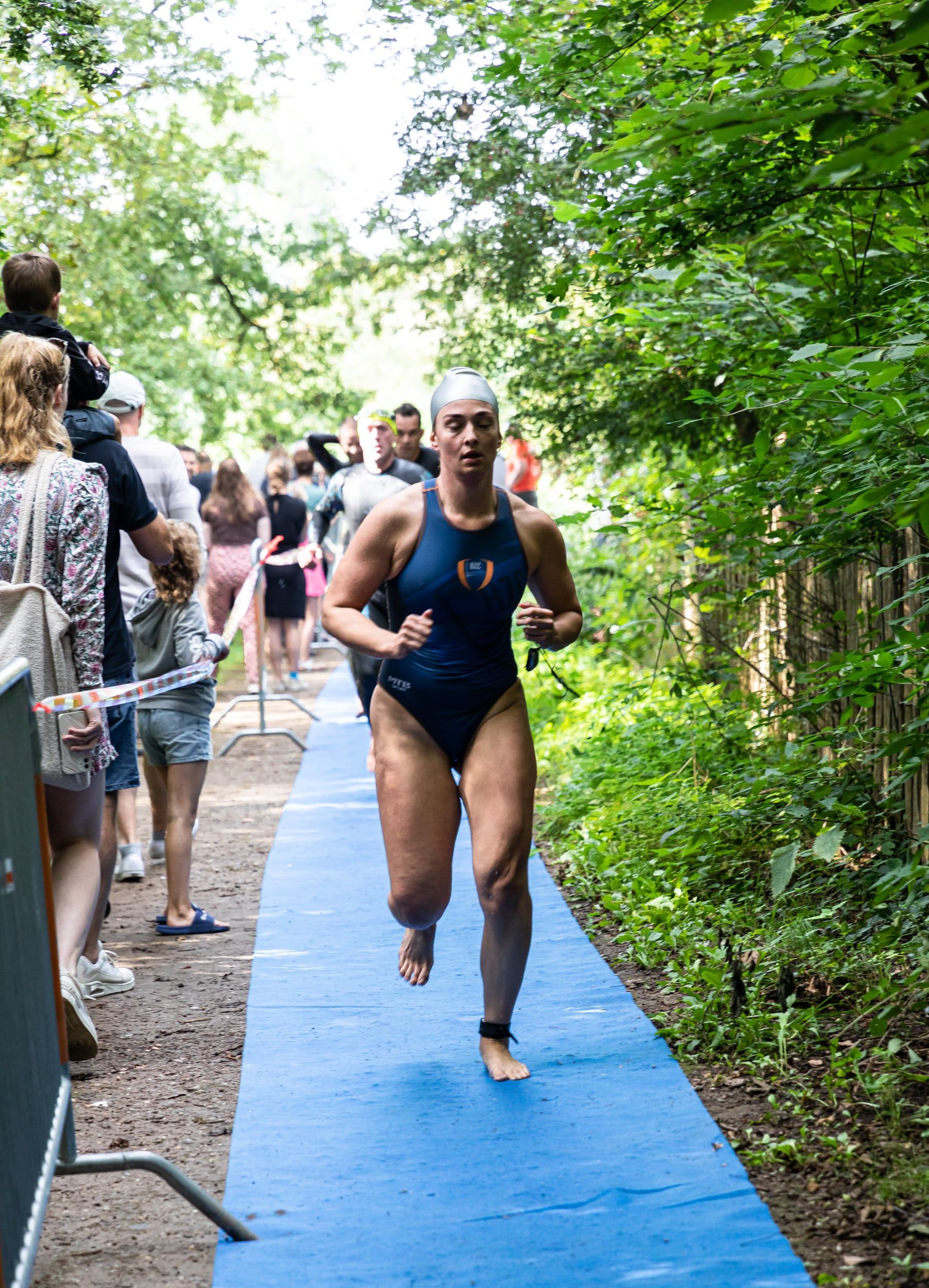 Een vrouw in een badpak rent op een blauwe mat in het bos.