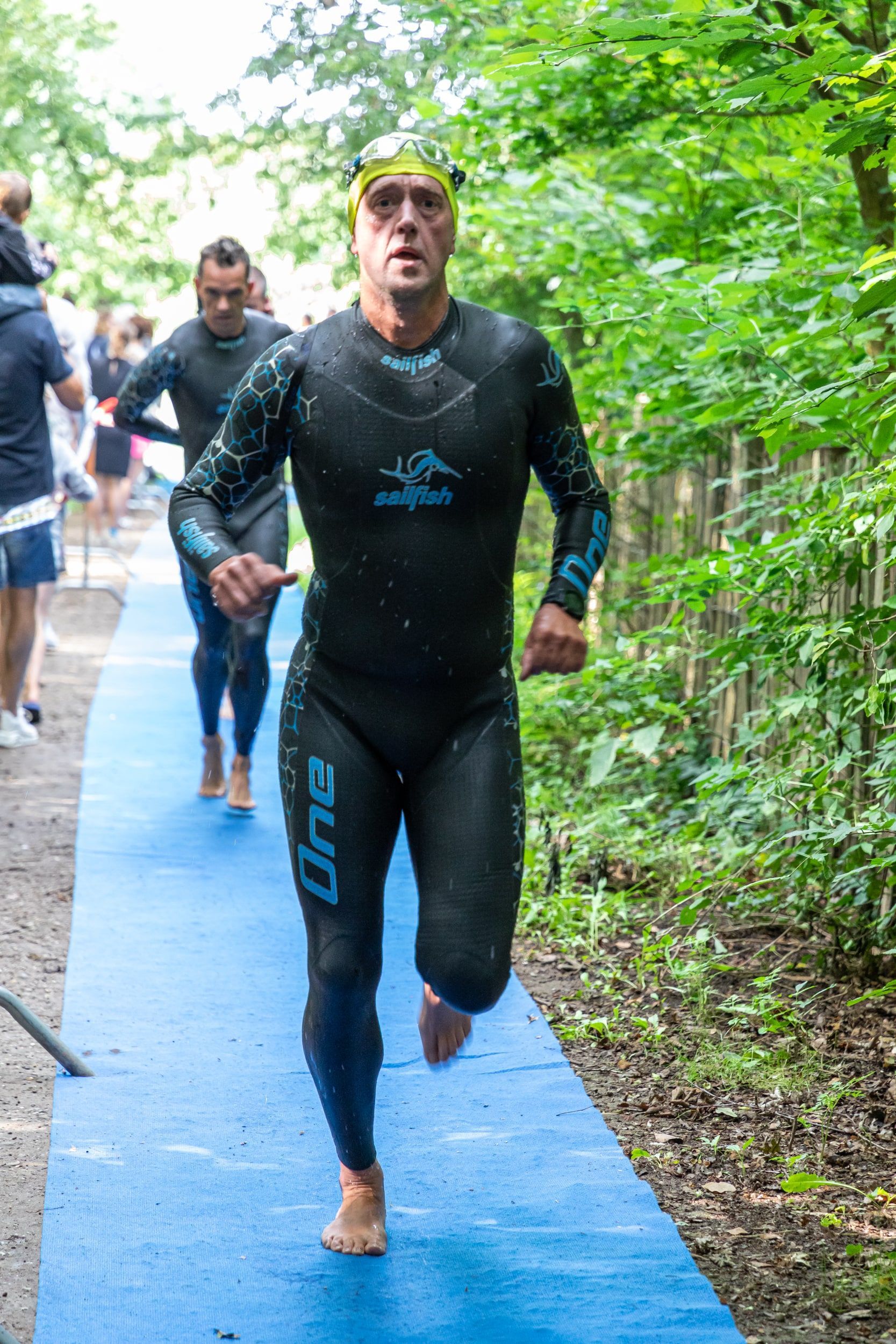 Een man in een wetsuit rent op een blauw pad.