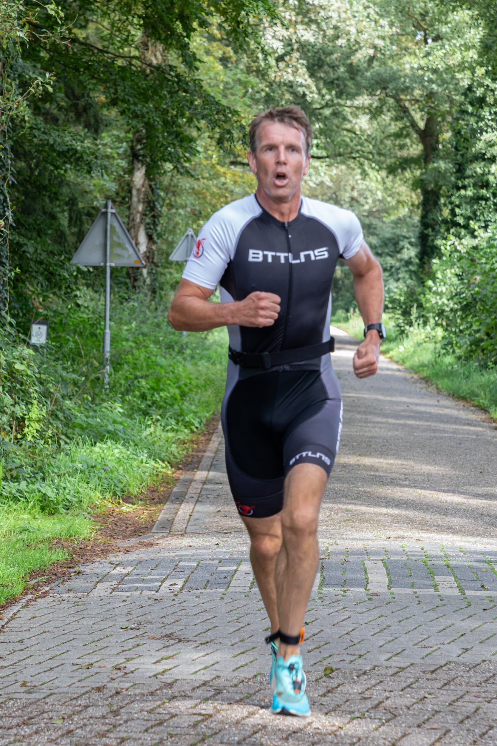 Een man in een triatlonpak rent over een stenen weg.