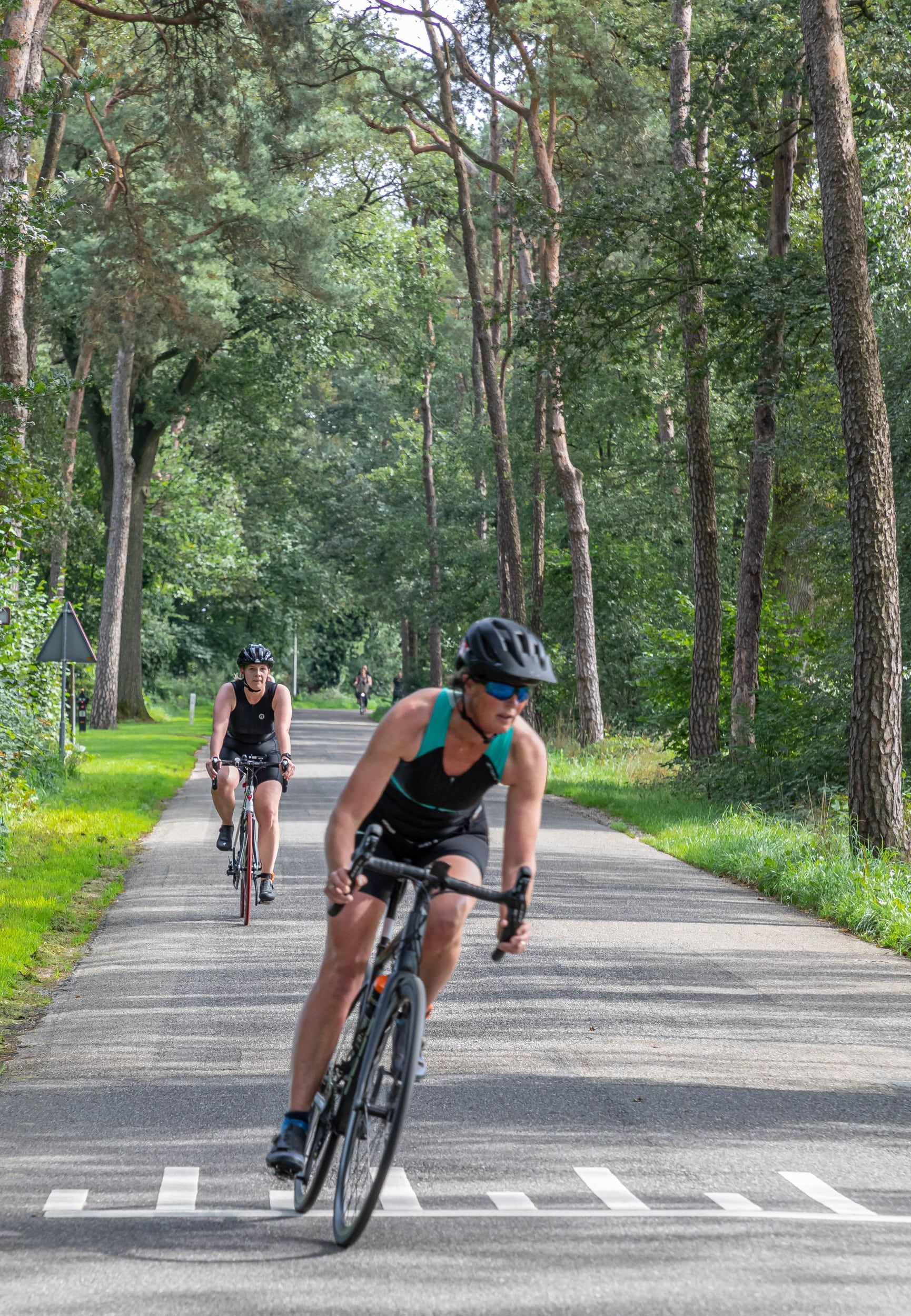 Twee mensen fietsen over een weg in het bos.