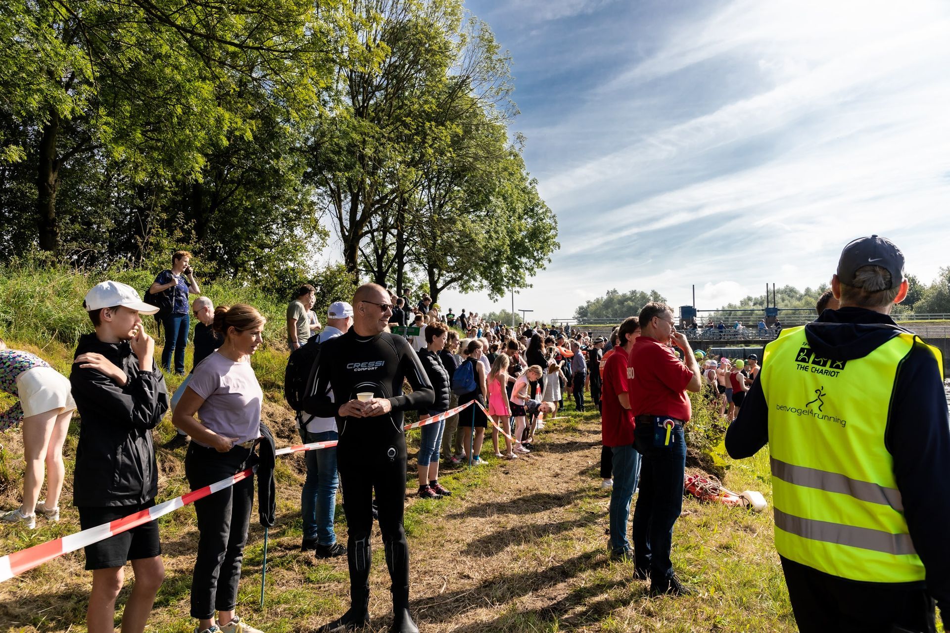 Een man in een geel vest staat voor een menigte mensen.