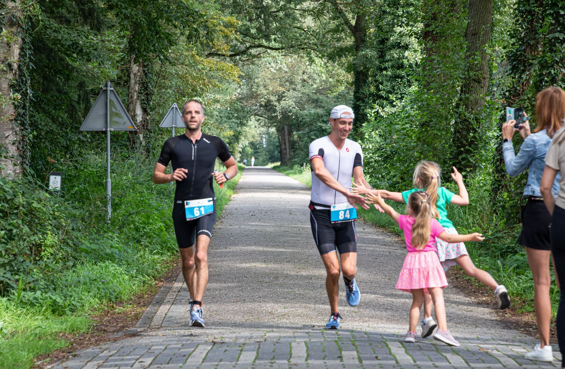 Twee mannen en een klein meisje rennen over een stenen weg.
