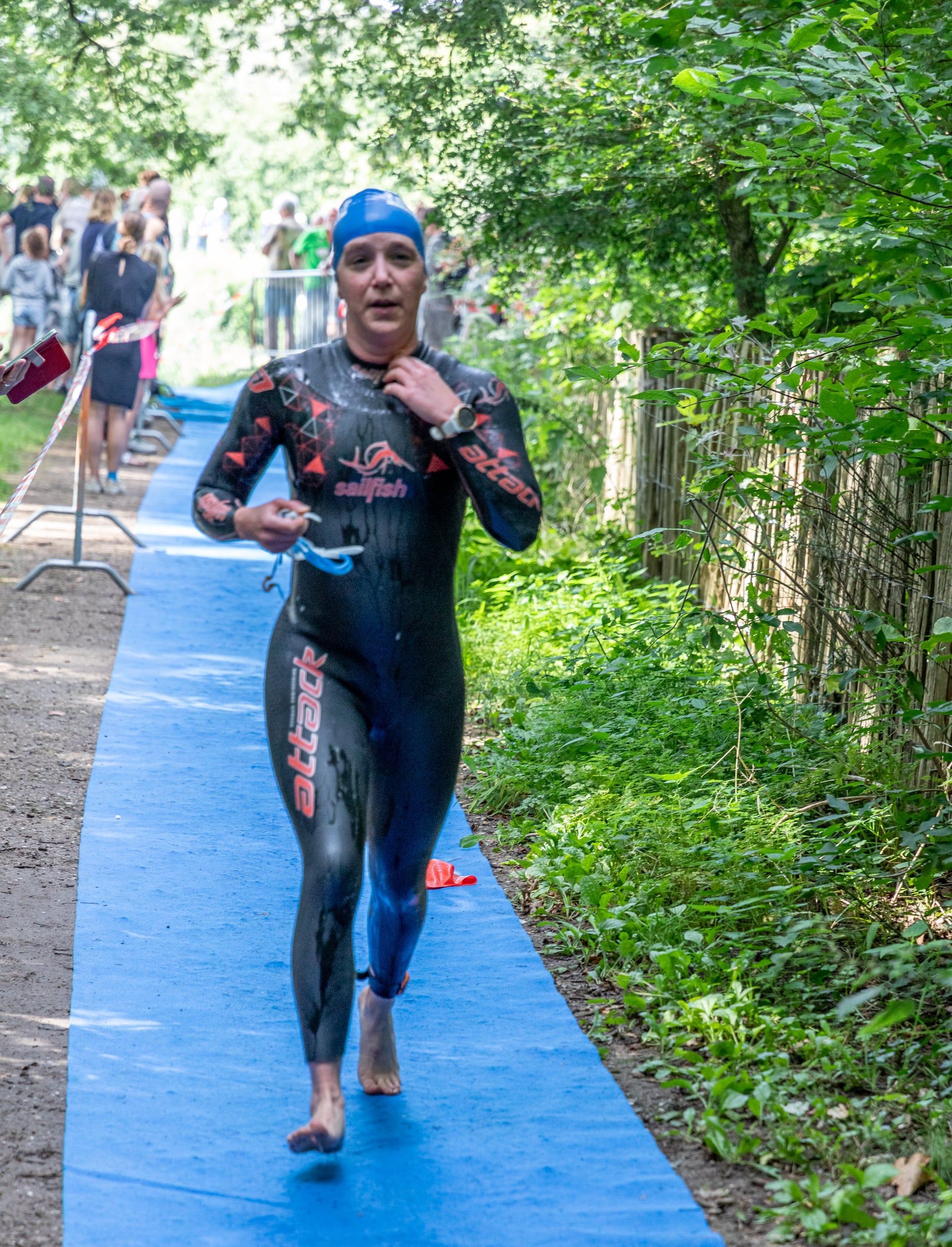 Een vrouw in een wetsuit rent op een blauw pad.