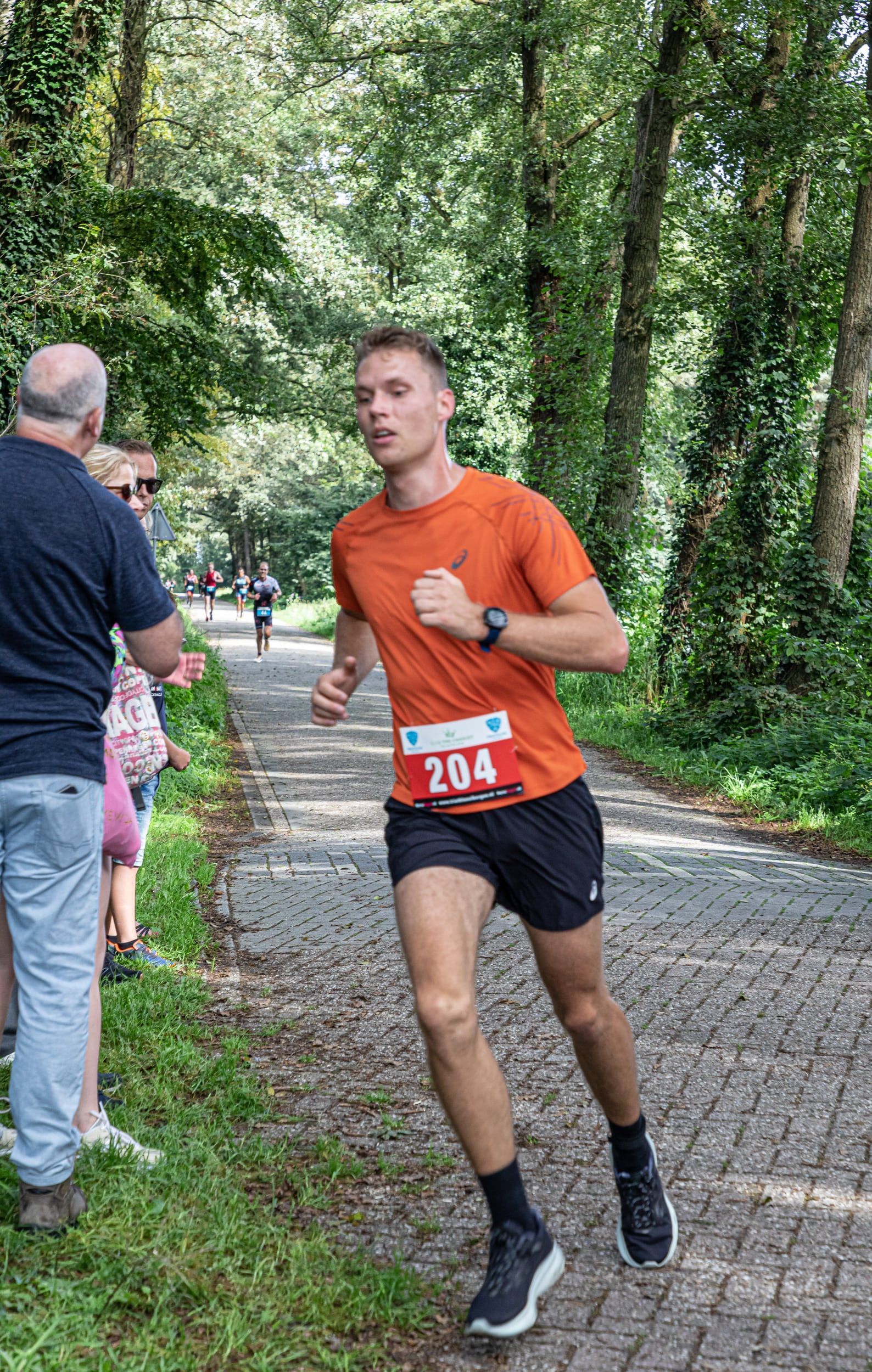 Een jongeman rent over een pad in het bos.