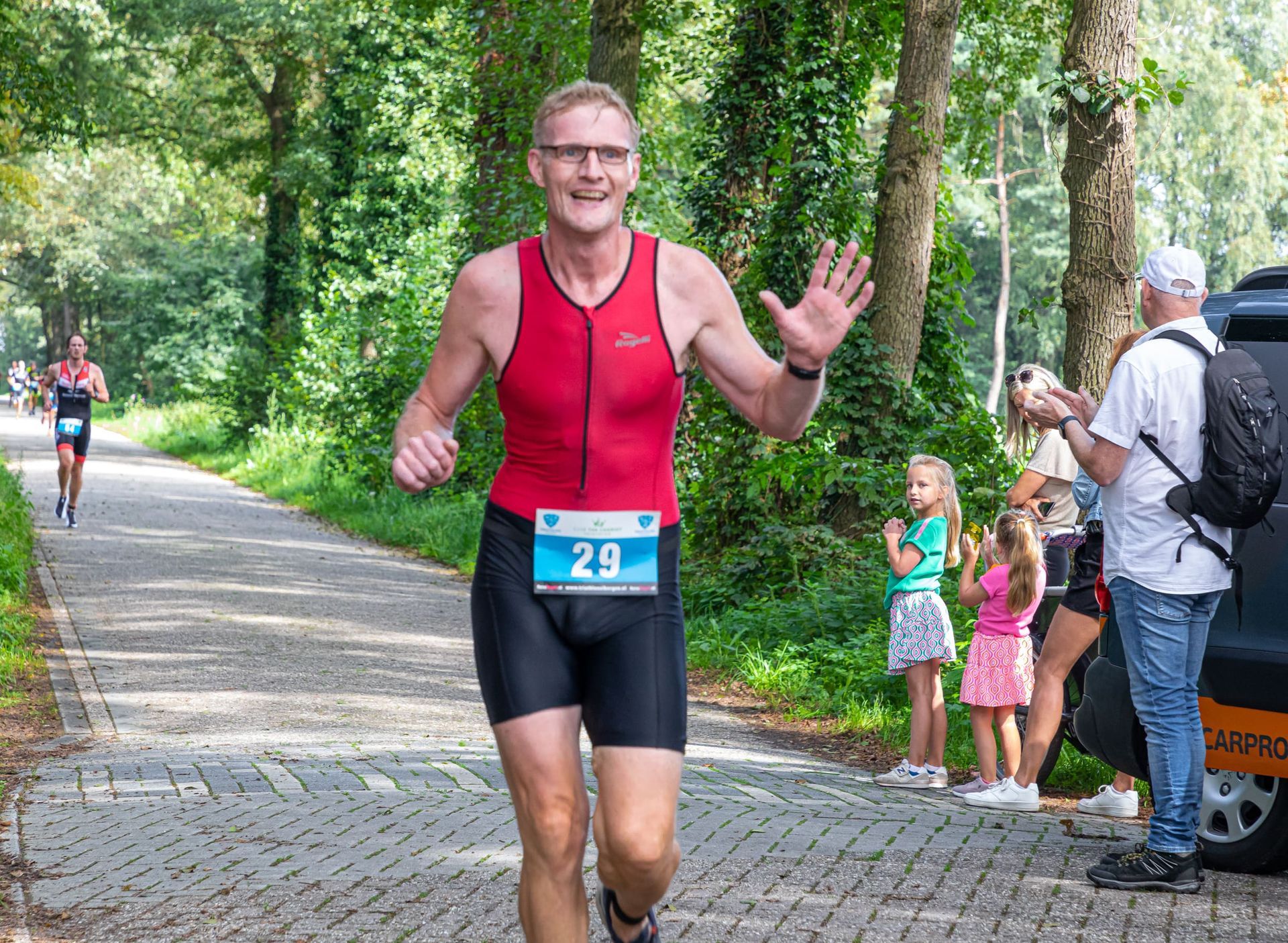 Een man in een rood tanktopje en een zwarte korte broek rent over de weg.