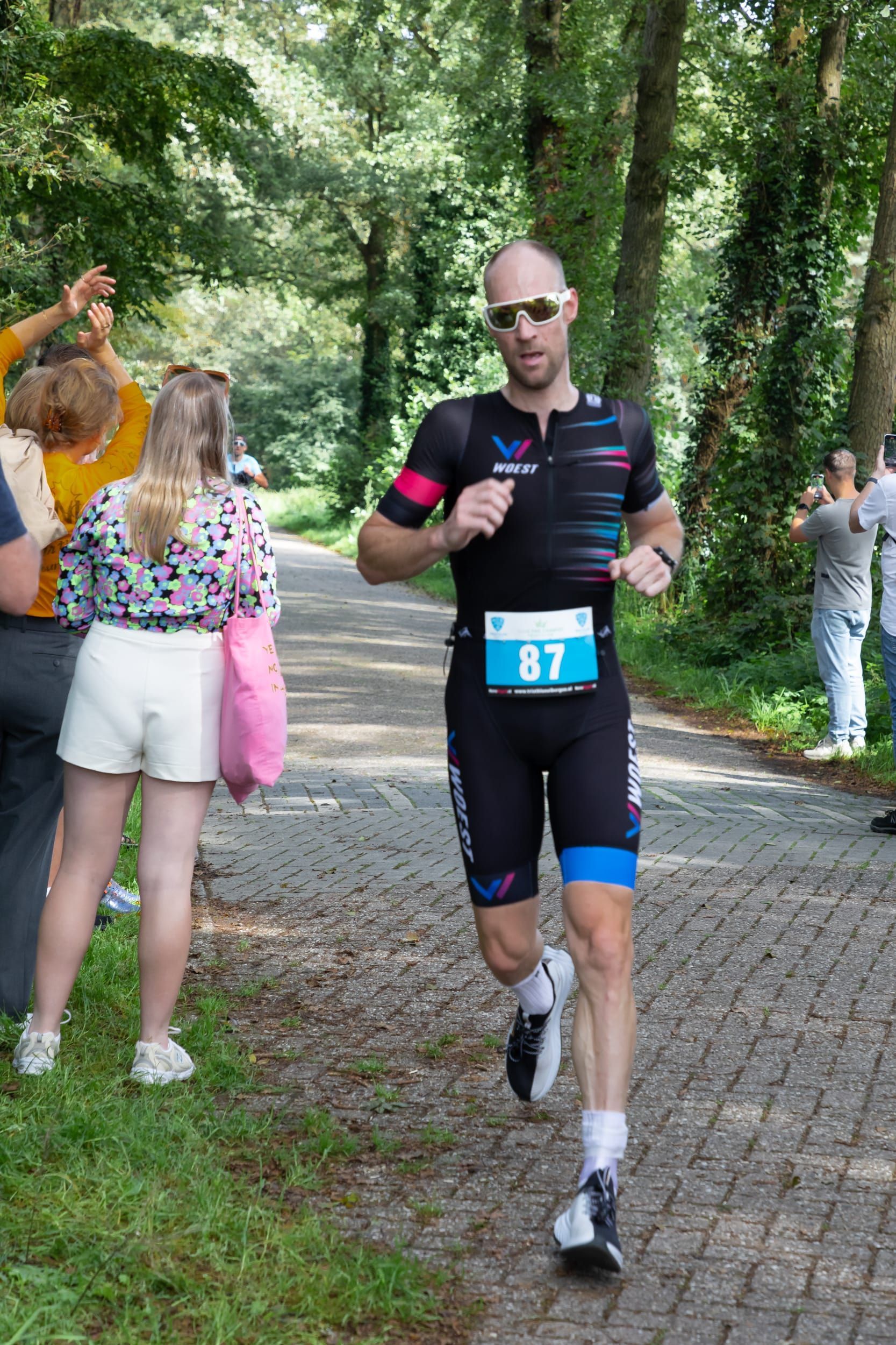 Een man in een triatlonpak rent over een geplaveide weg.