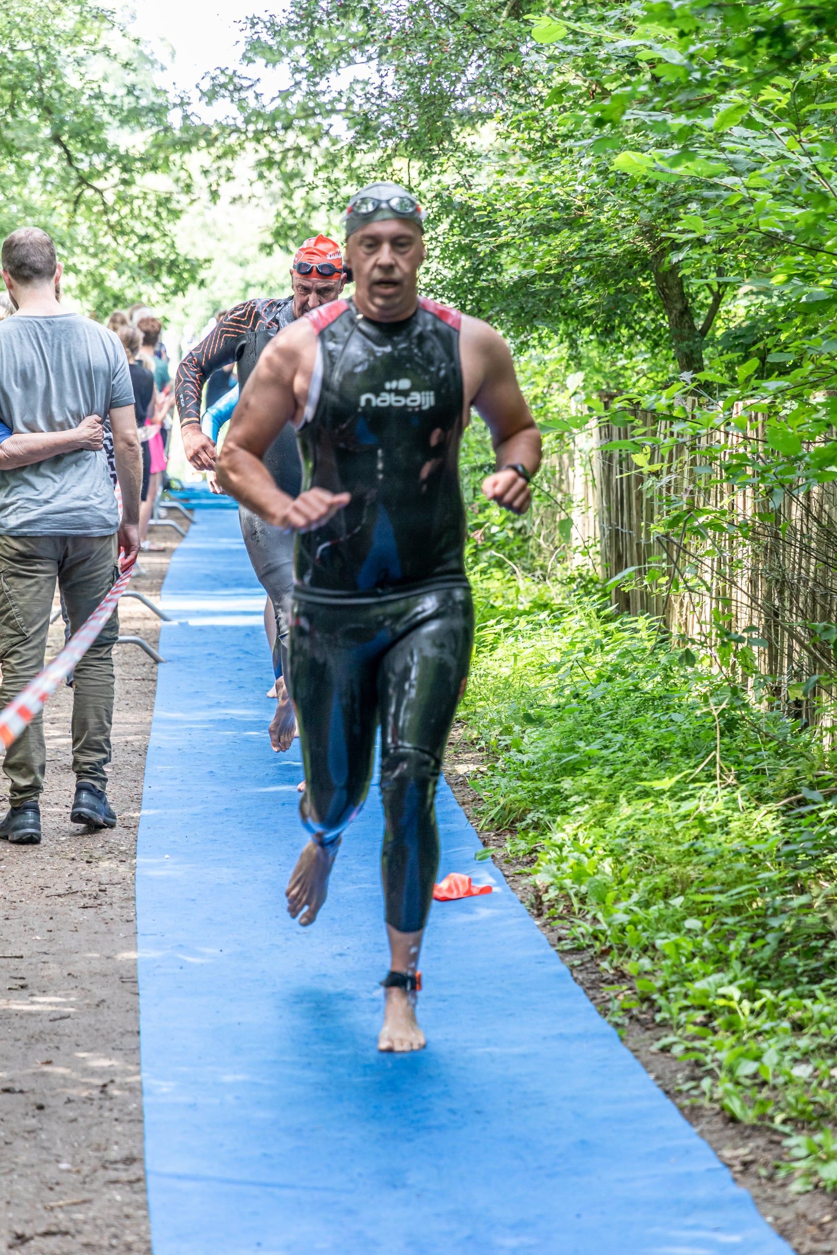 Een man in een wetsuit rent over een pad.