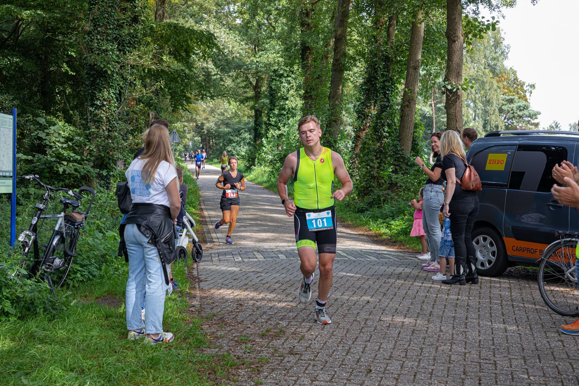 Een groep mensen staat langs de kant van de weg en kijkt naar een rennende man.