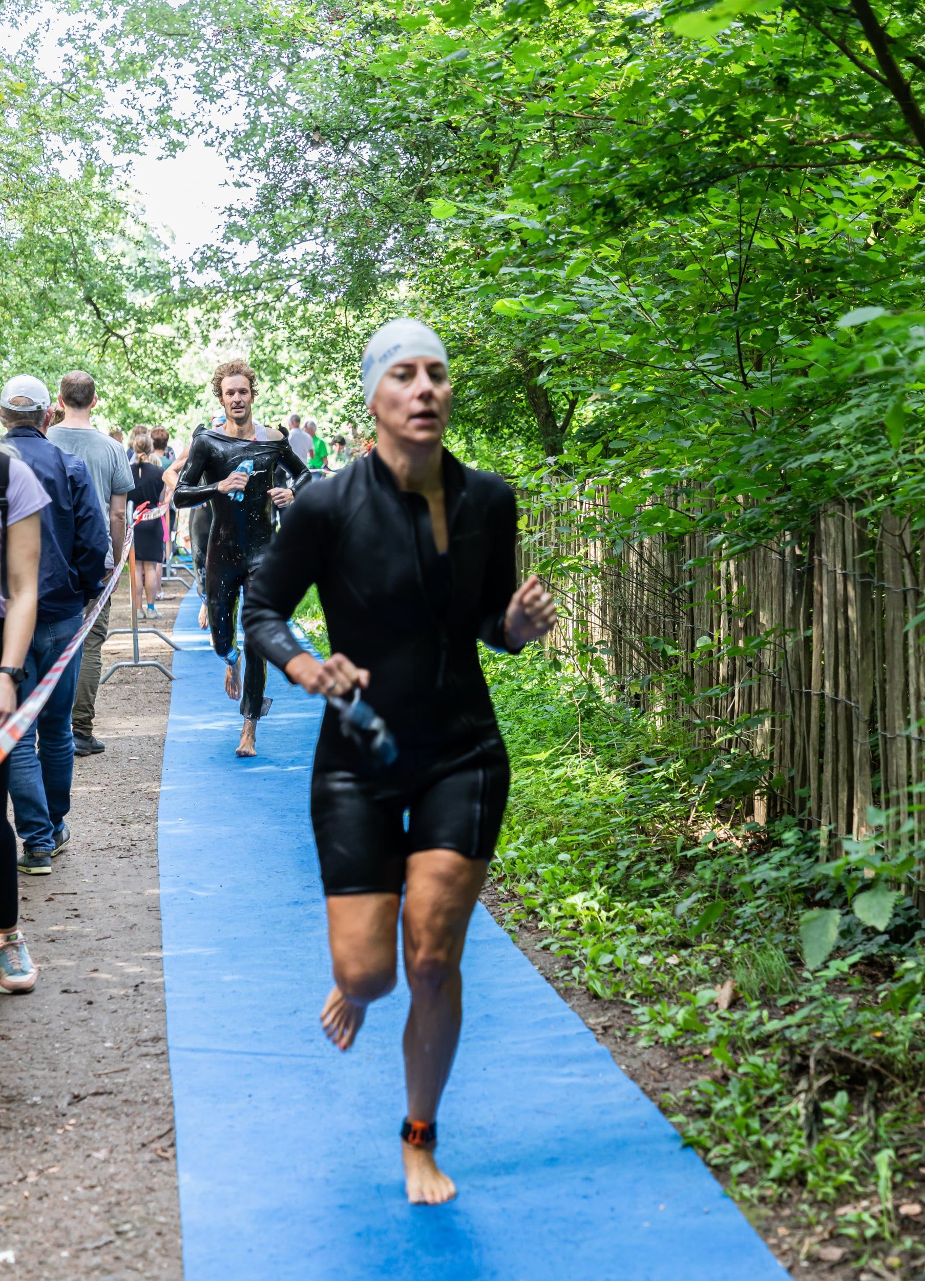Een vrouw in een wetsuit rent op een blauwe mat in het bos.