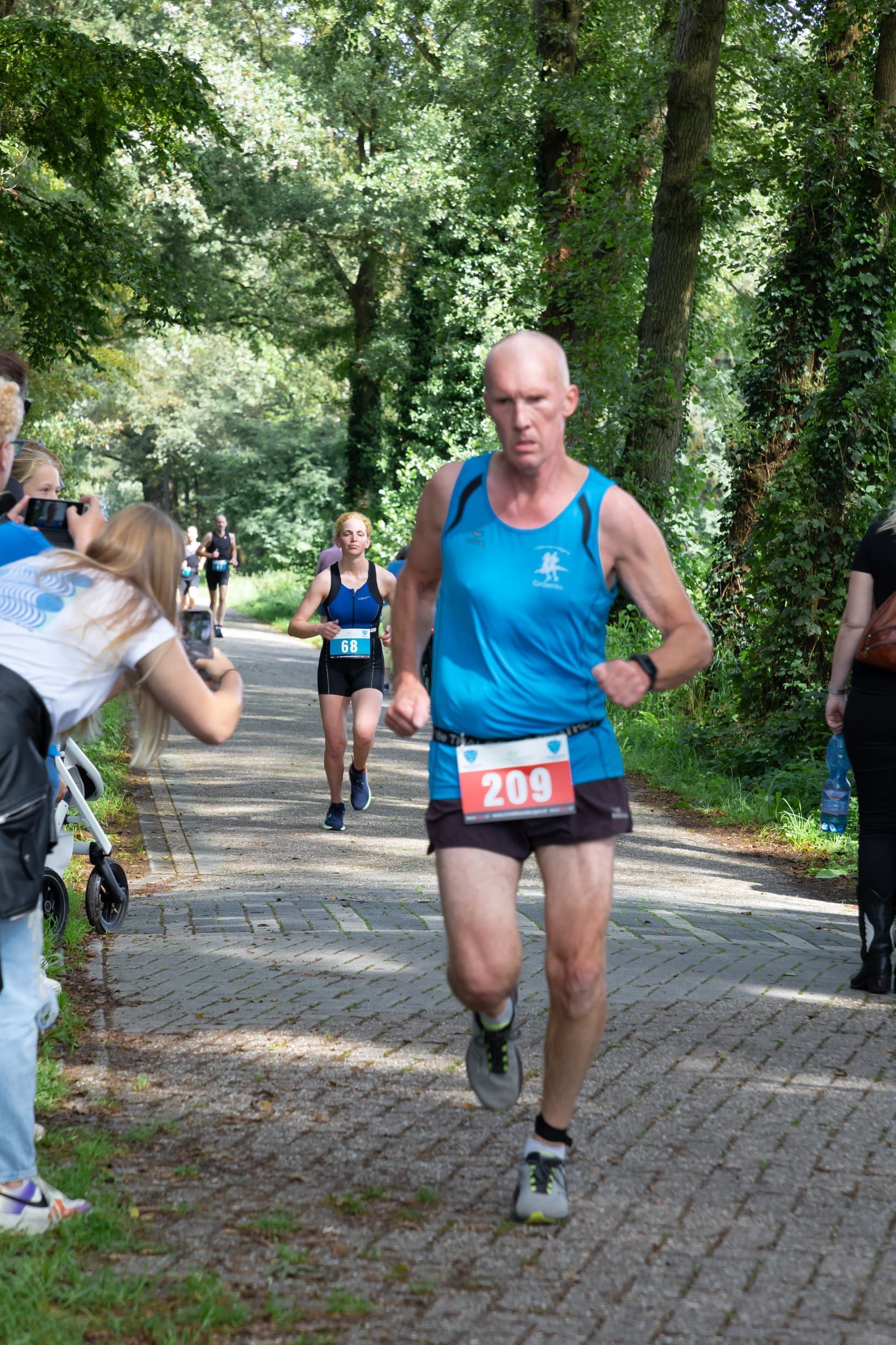 Een man in een blauw tanktopje rent over een pad.