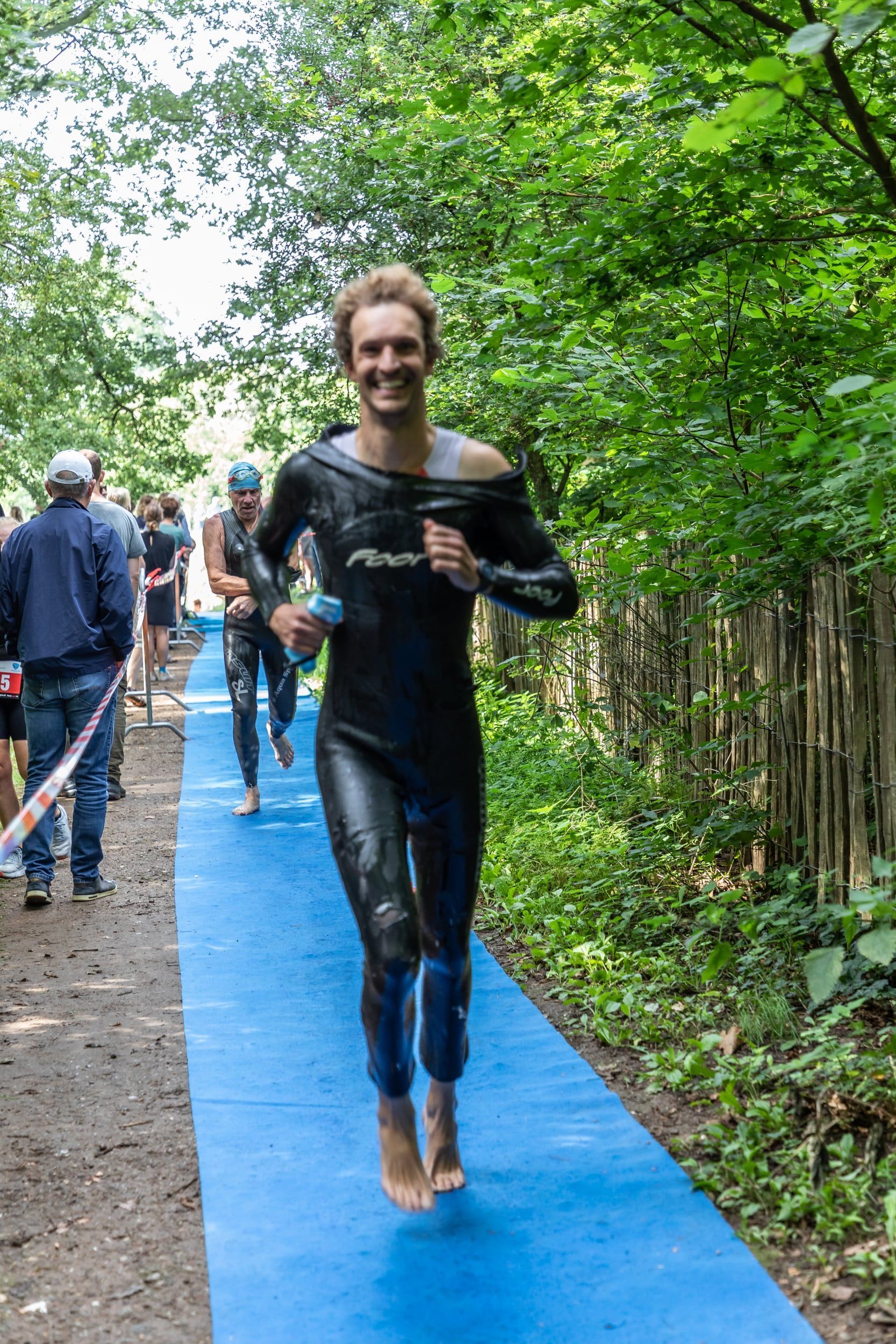 Een man in een wetsuit rent op een blauwe mat in het bos.
