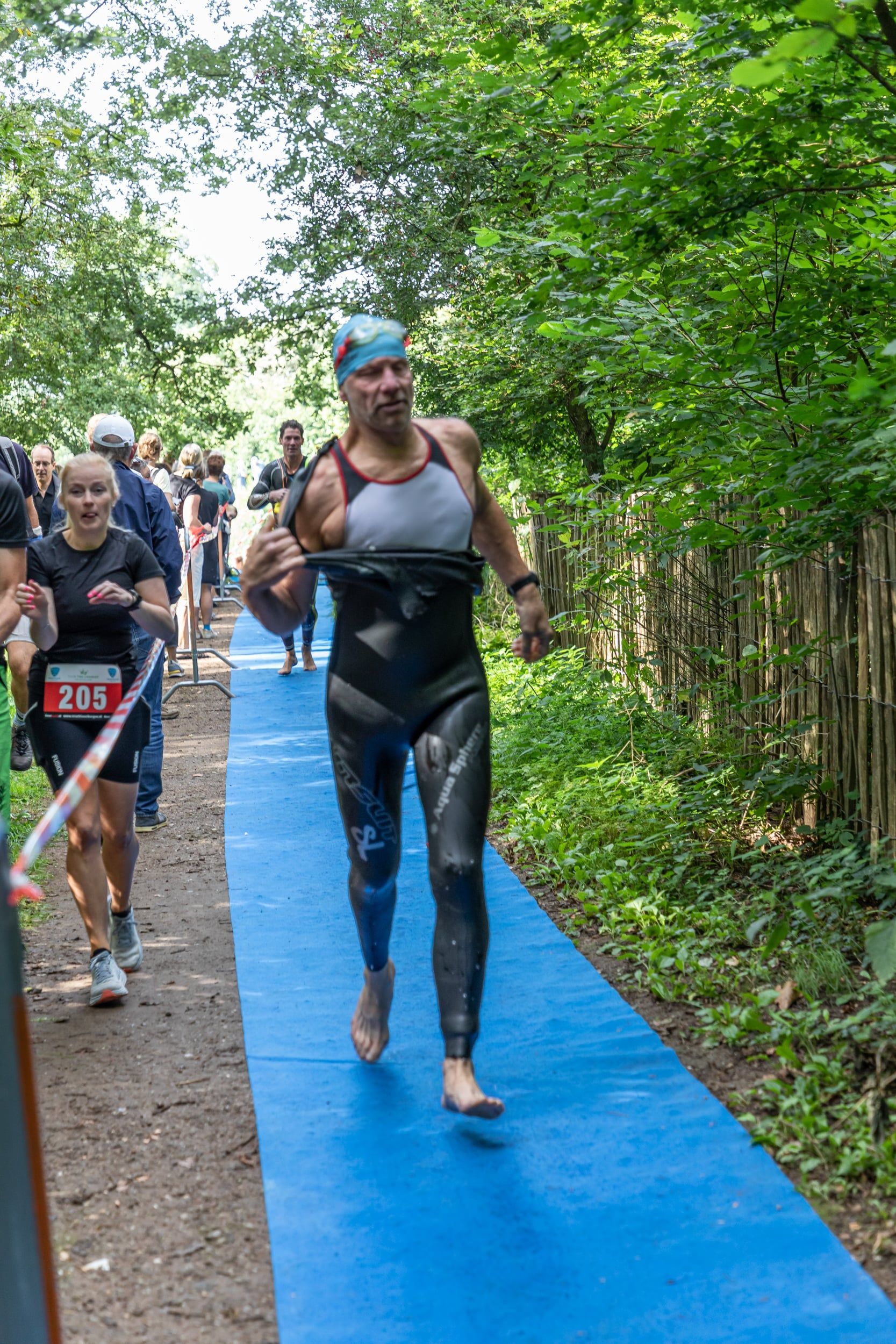 Een man in een wetsuit rent op een blauwe mat in het bos.