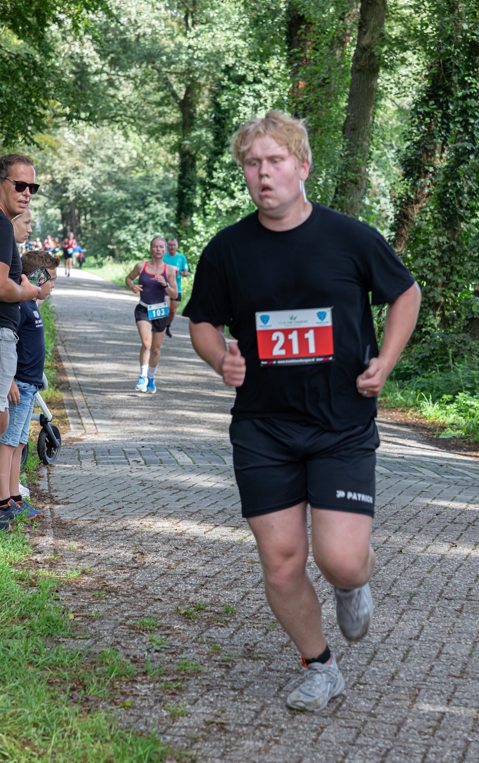 Een man in een zwart shirt en korte broek rent over een pad.