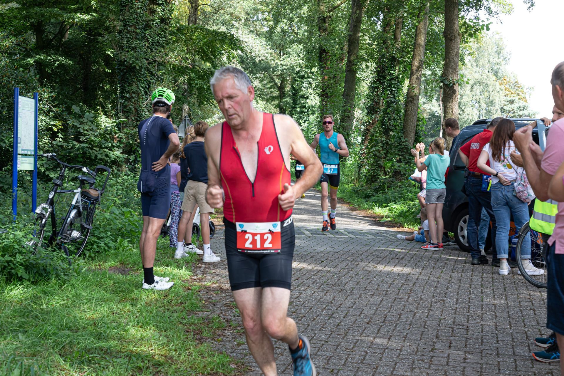 Een man in een rood shirt en een zwarte korte broek rent over een geplaveide weg.