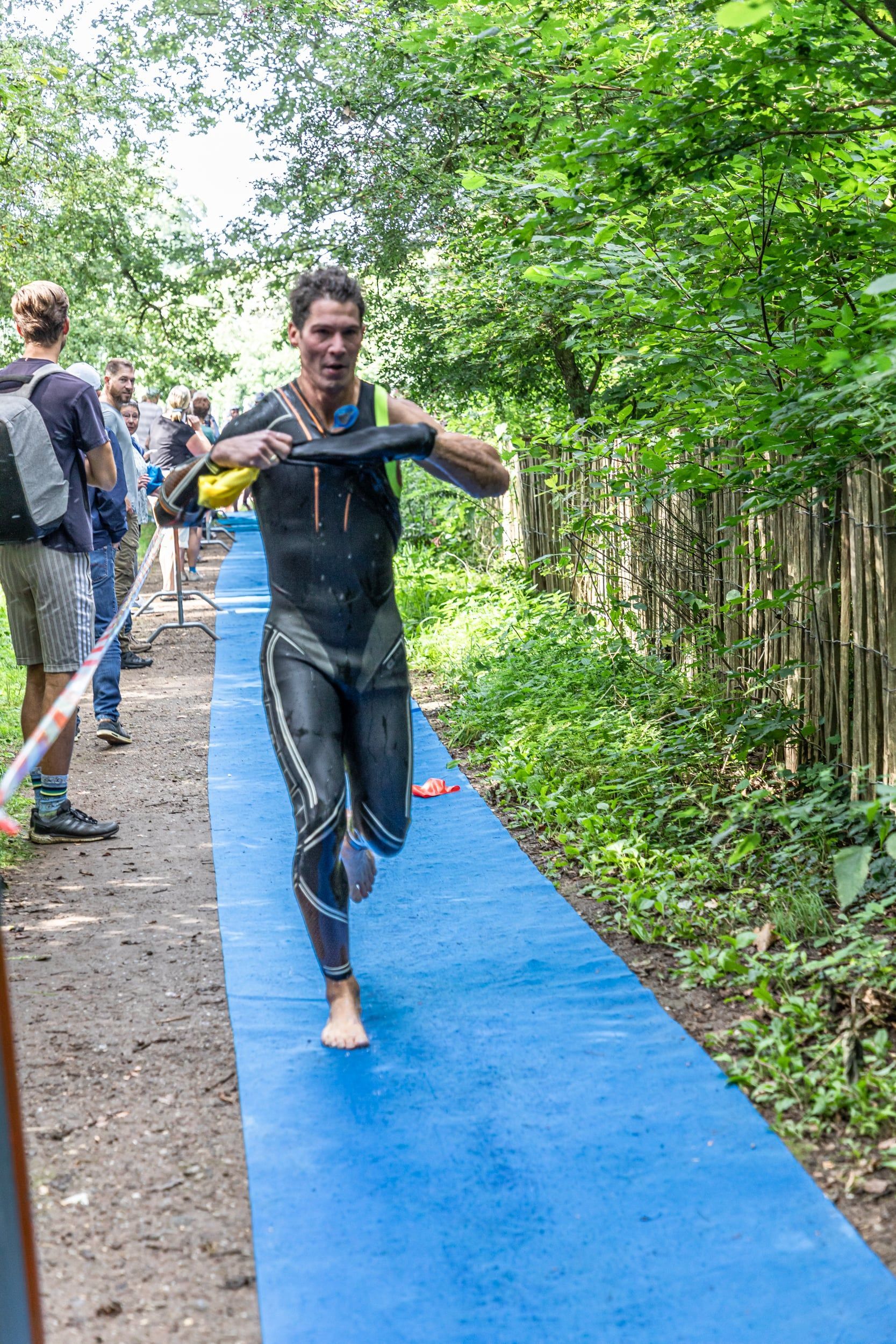Een man in een wetsuit rent op een blauwe loper.