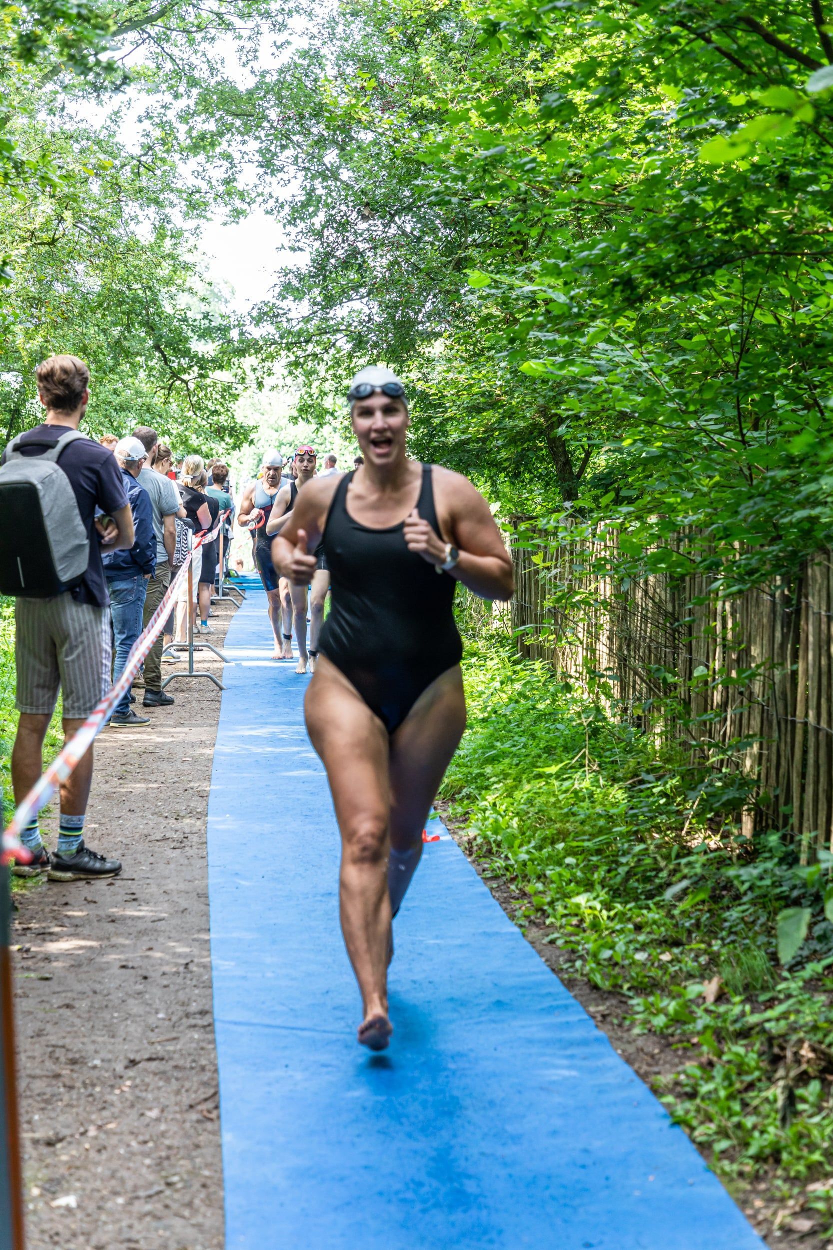 Een vrouw in een badpak rent op een blauw pad in het bos.