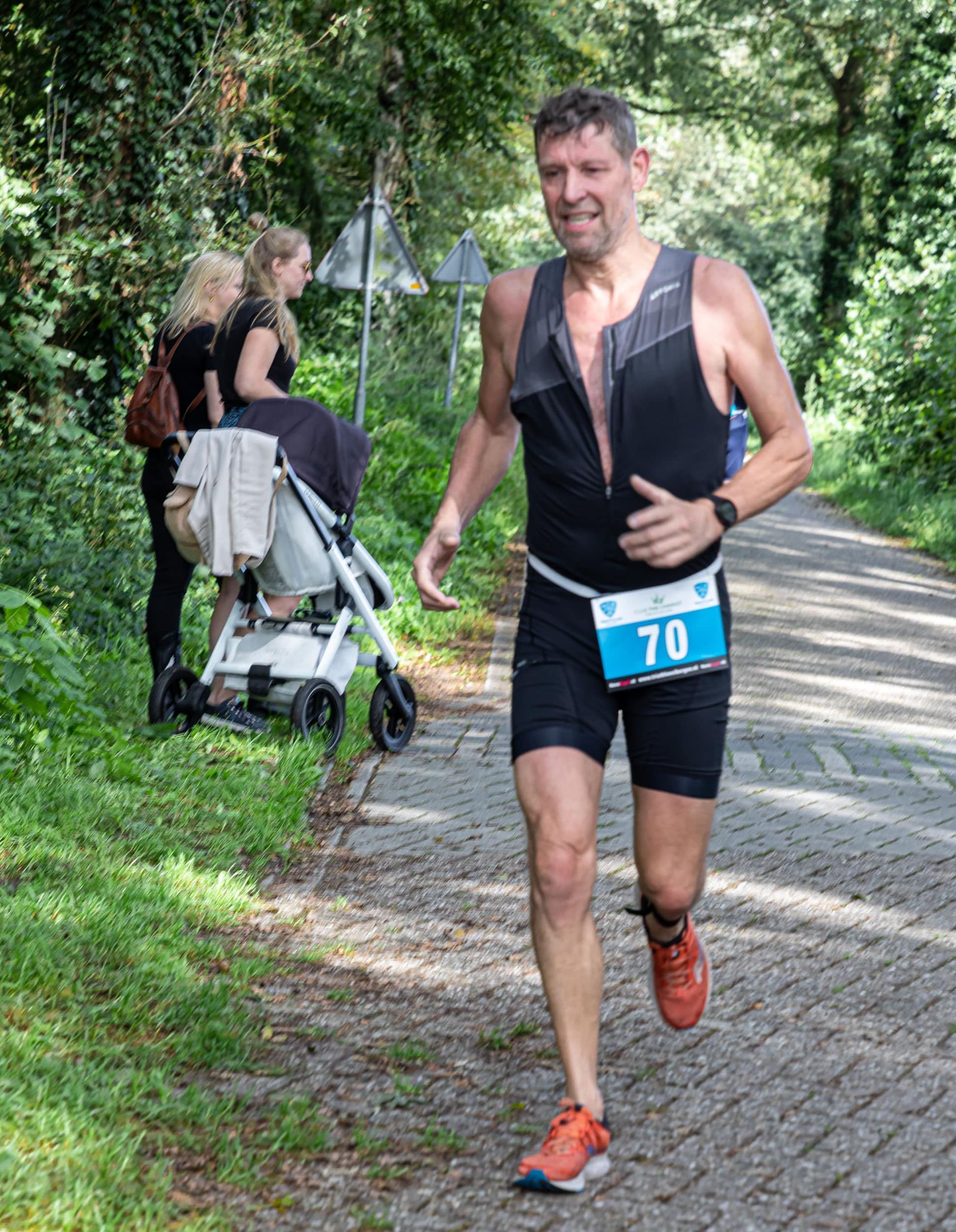 Een man rent over de weg, met op de achtergrond een kinderwagen.