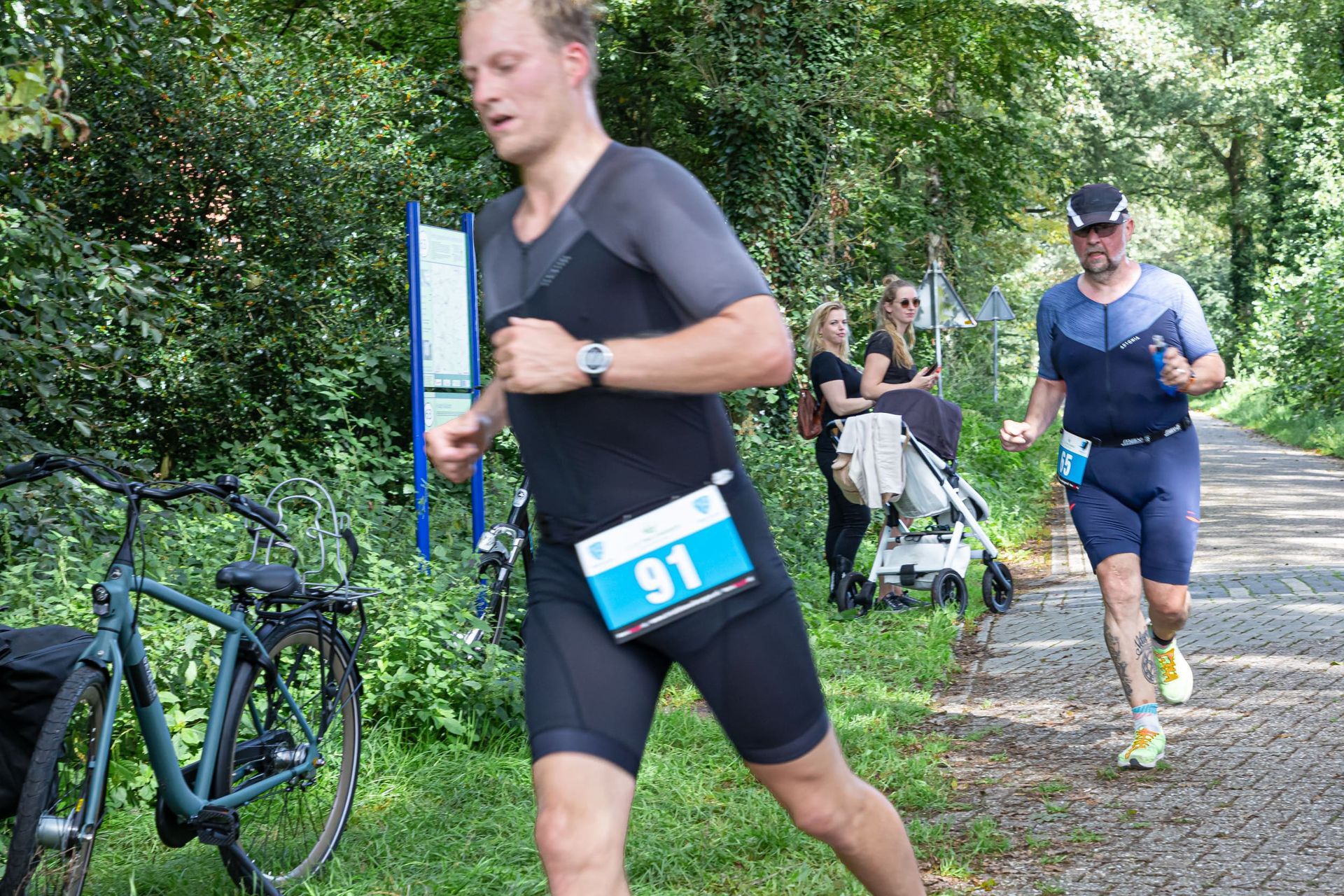 Een man rent op een pad, met op de achtergrond een fiets en een kinderwagen.
