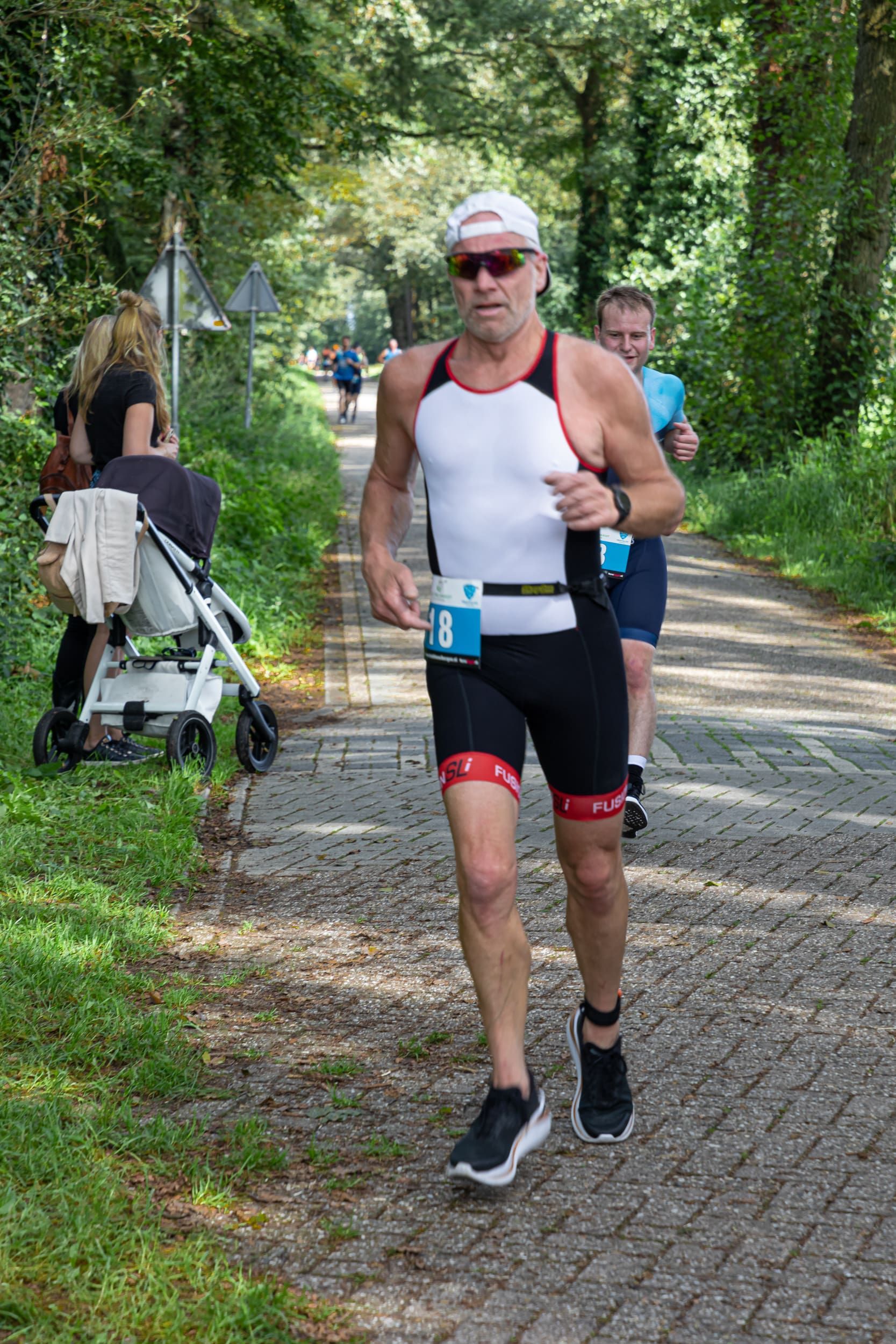 Een man rent over een pad naast een kinderwagen.