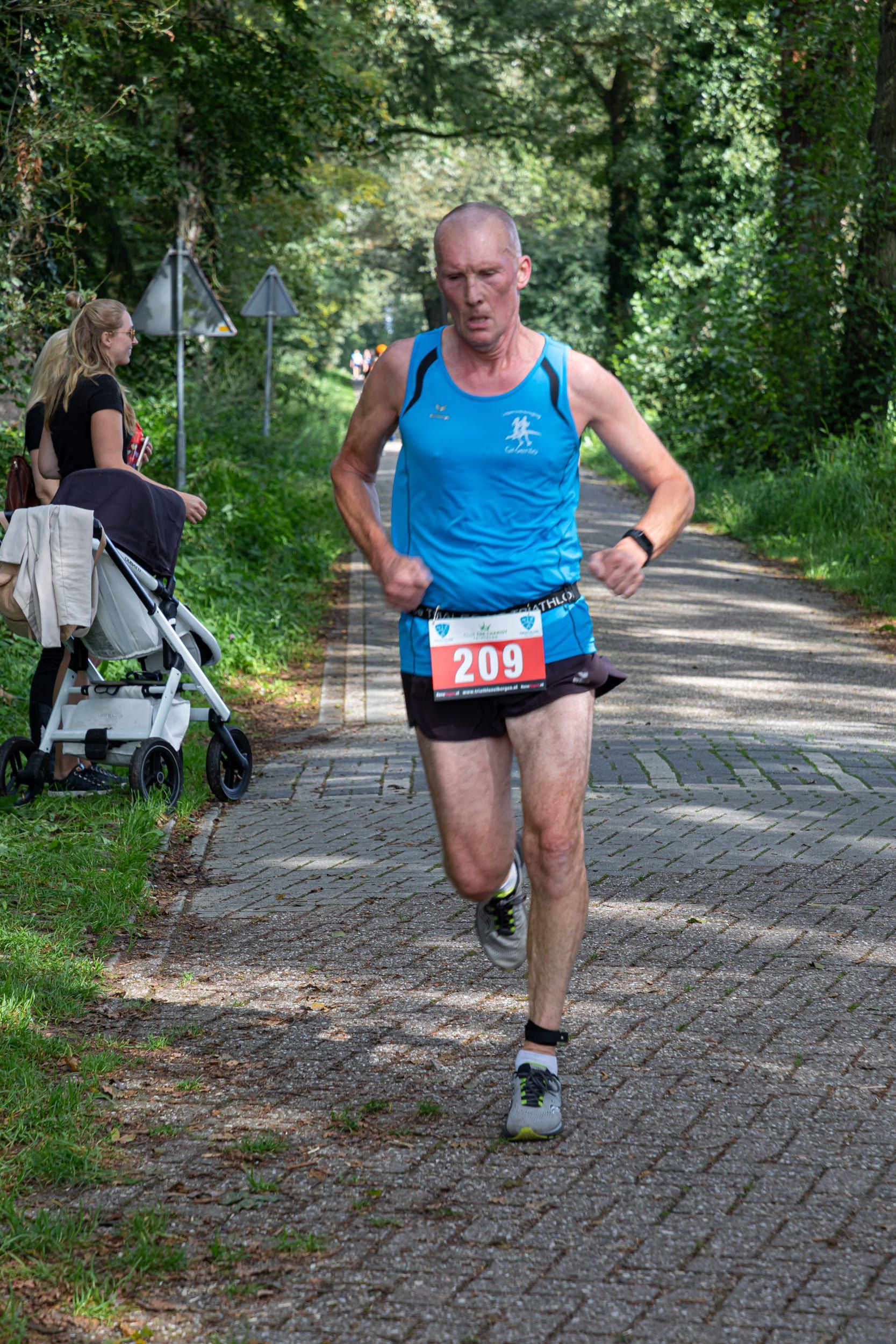 Een man in een blauw tanktopje en korte broek rent over de weg.