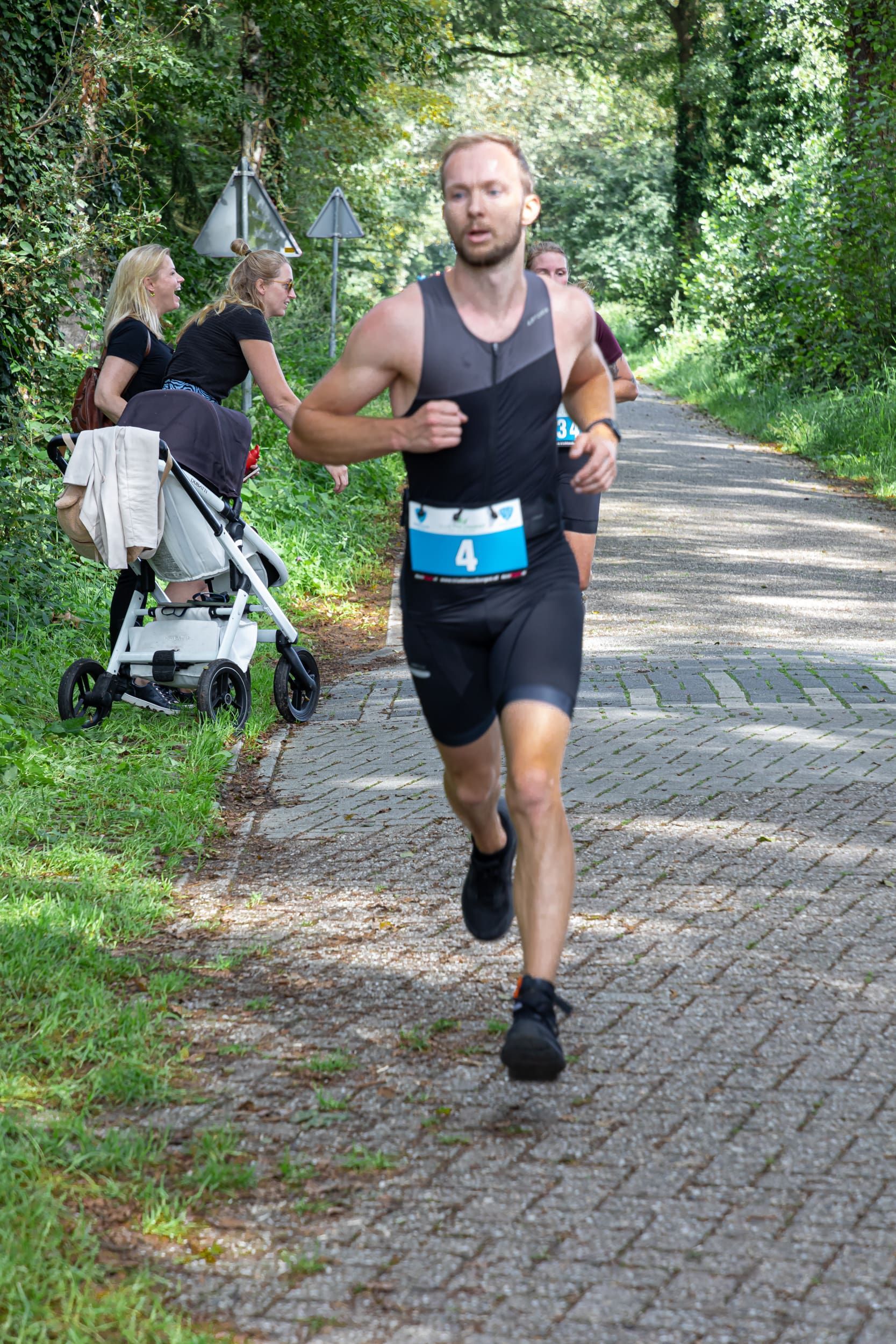 Een man rent over een stenen weg, met op de achtergrond een kinderwagen.