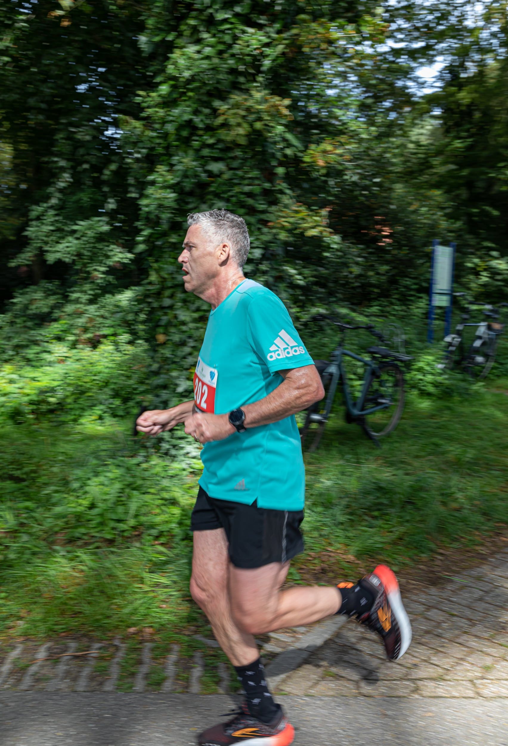 Een man in een groen shirt en een zwarte korte broek rent over de weg.