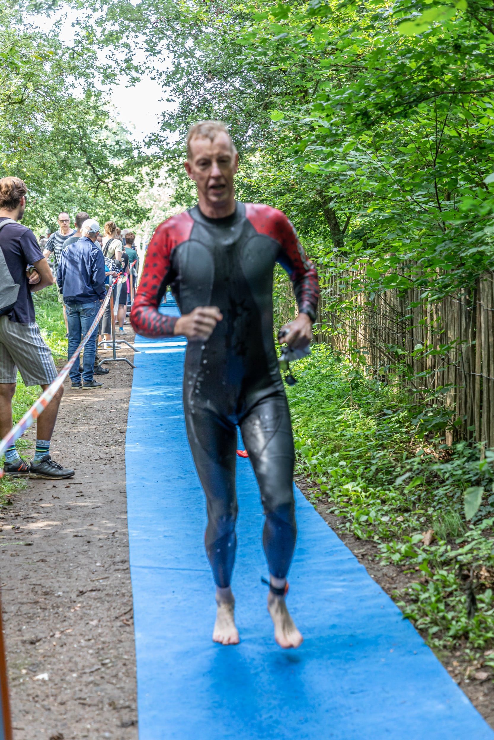 Een man in een wetsuit rent op een blauwe mat.