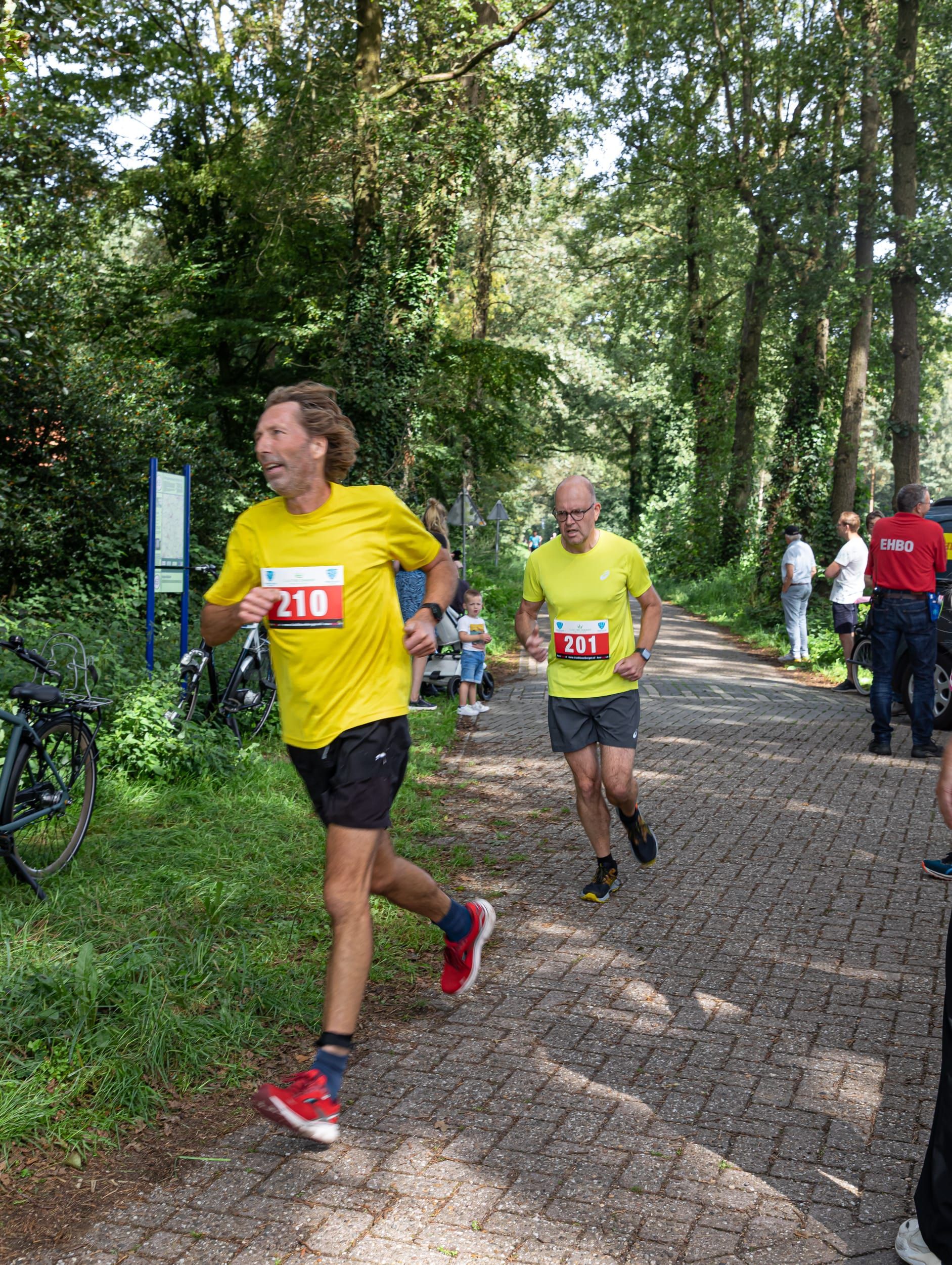 Een man in een geel shirt rent over een geplaveide weg.
