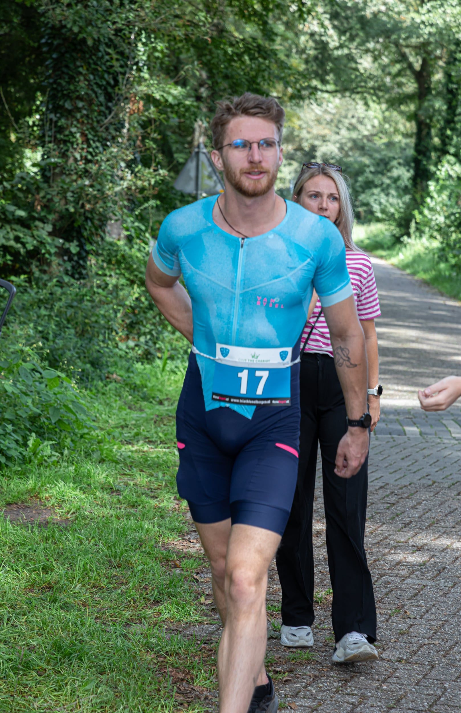 Een man in een blauw shirt en een korte broek loopt over een pad.