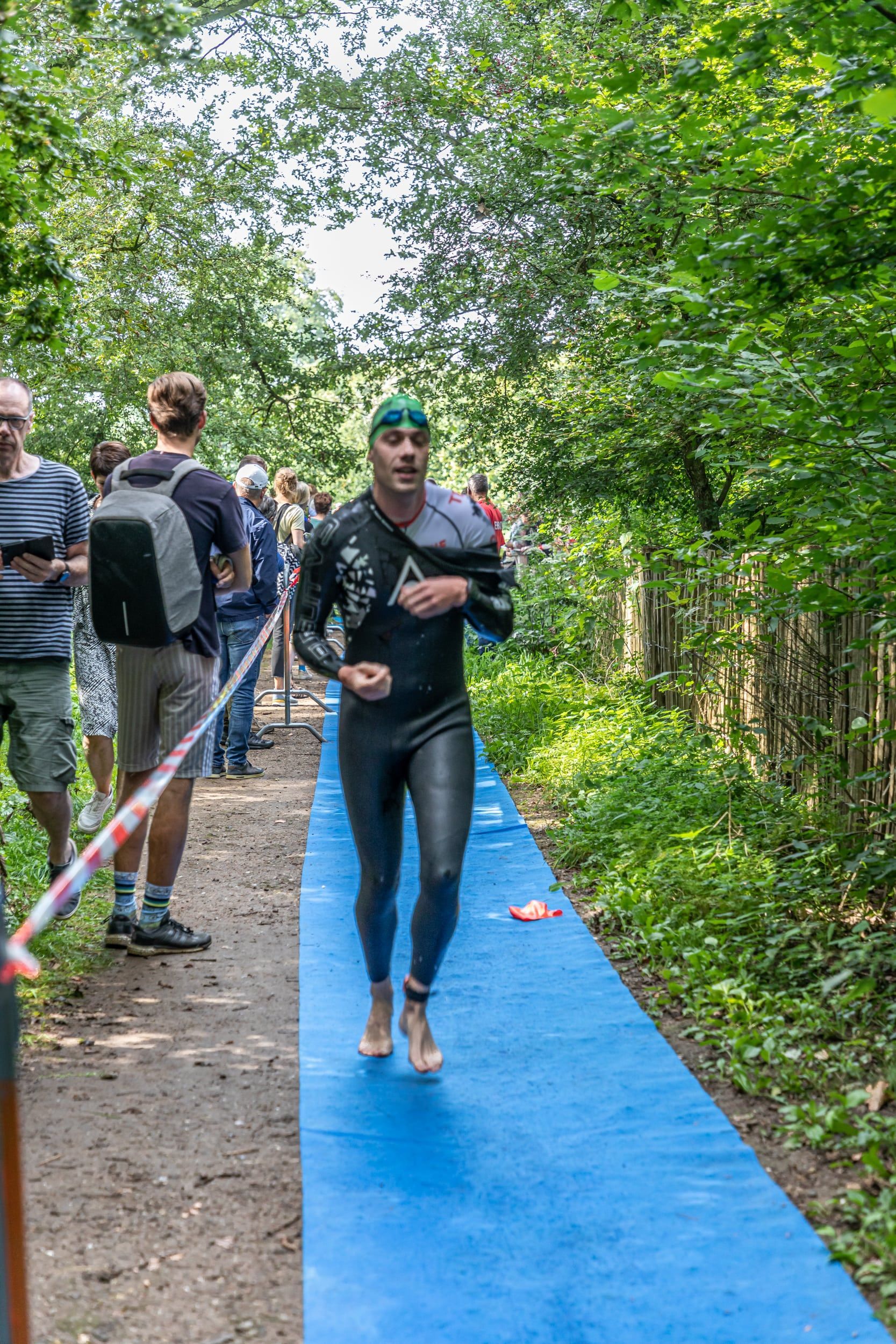 Een man in een wetsuit rent over een pad in het bos.