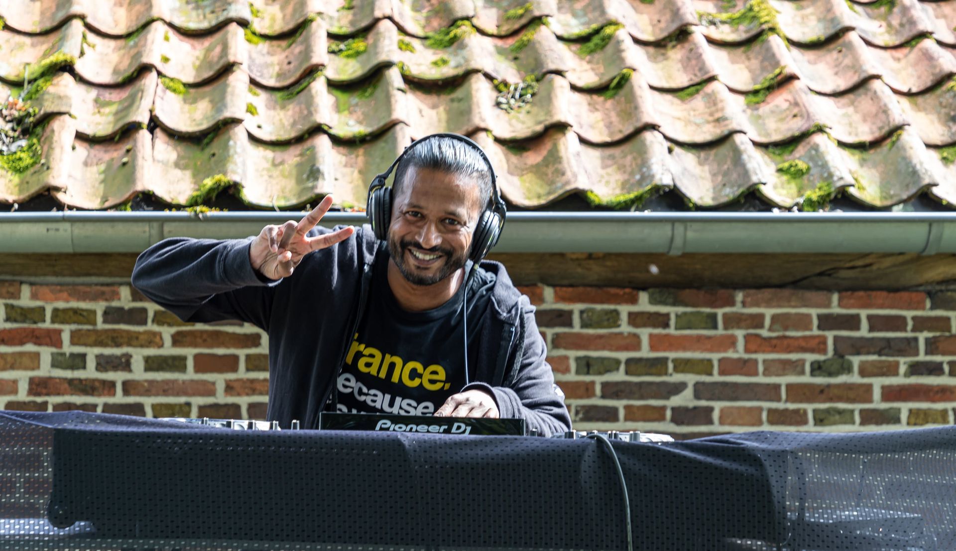 Prijsuitreiking Triathlon Eibergen 2023. Een man met een koptelefoon staat voor een bakstenen gebouw.