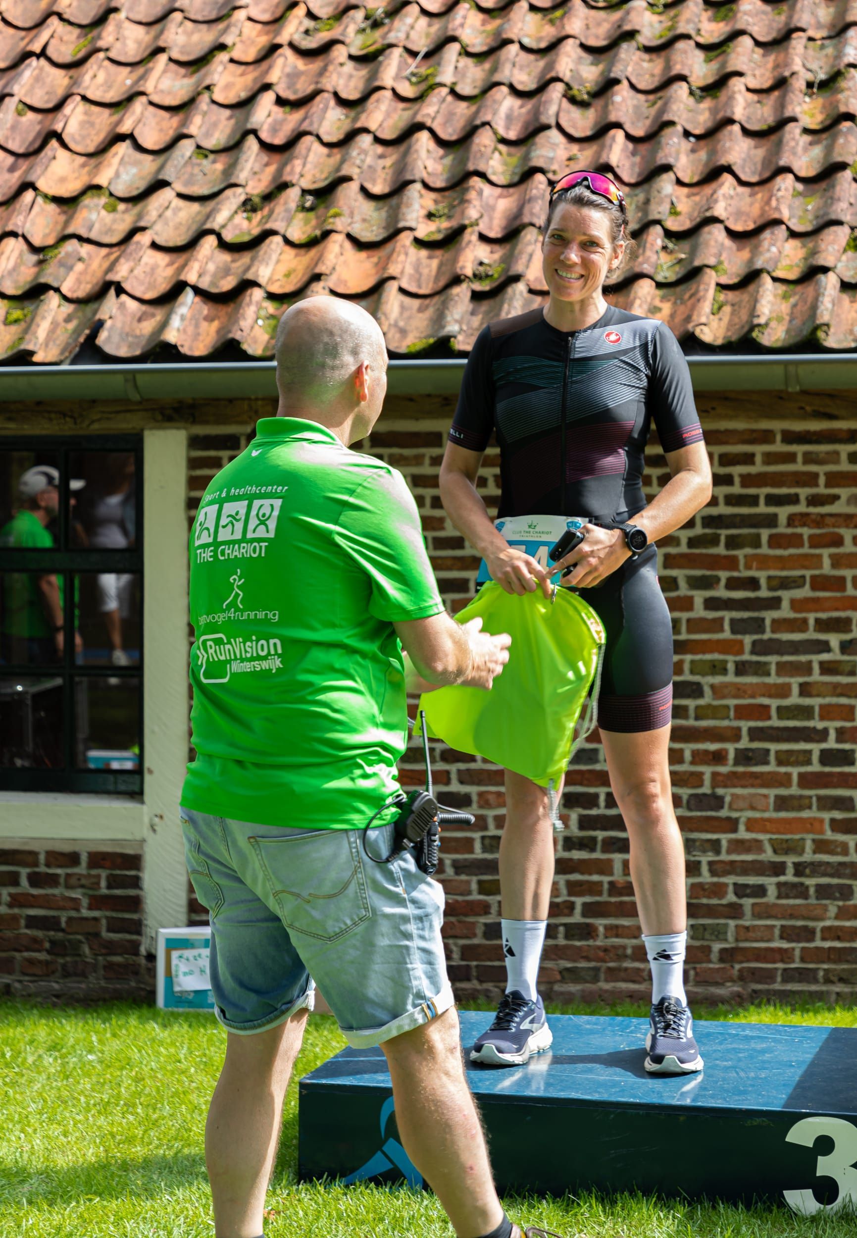 Prijsuitreiking Triathlon Eibergen 2023. Een man in een groen shirt staat naast een vrouw op een podium.