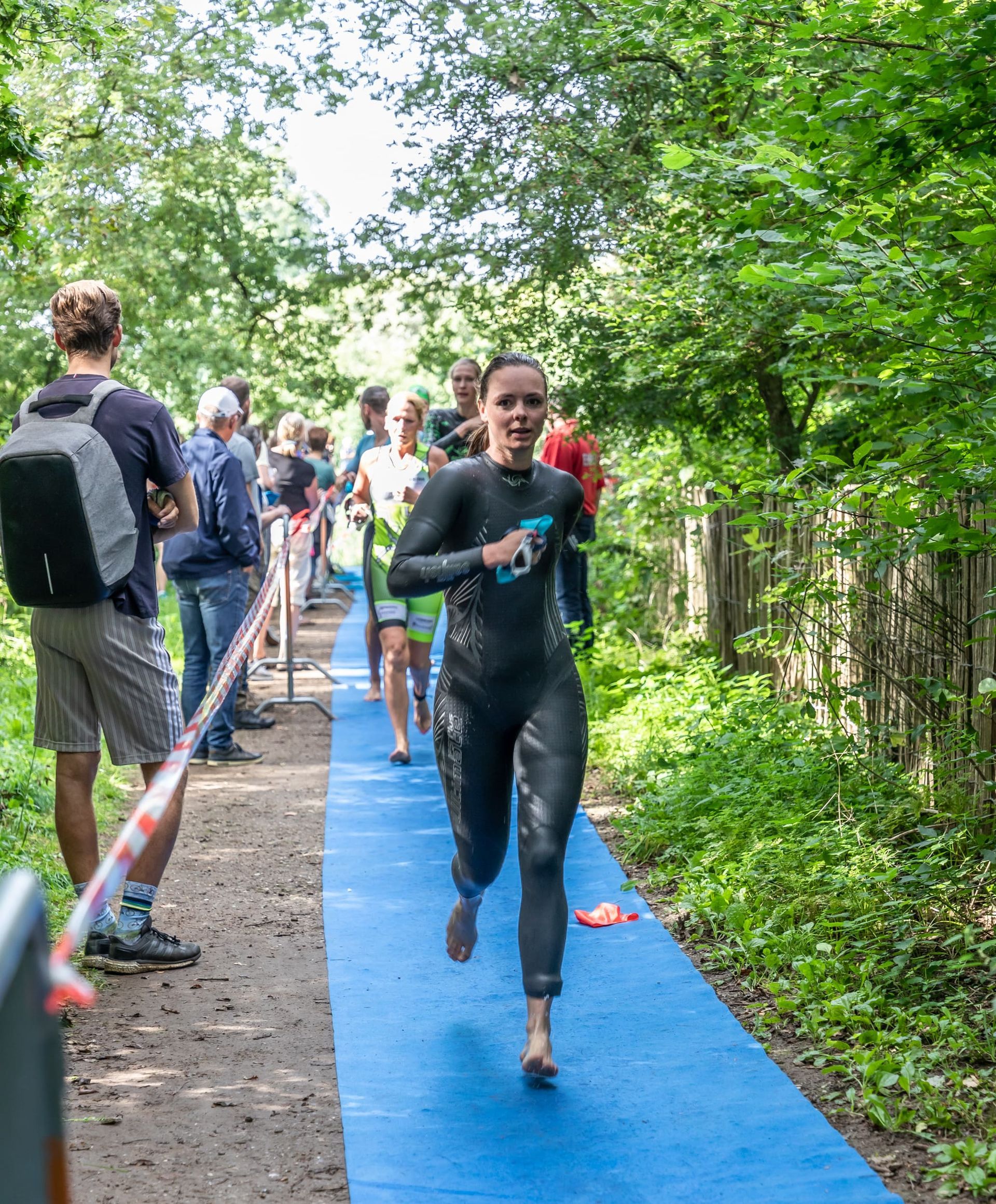 Een vrouw in een wetsuit rent op een blauw pad in het bos.