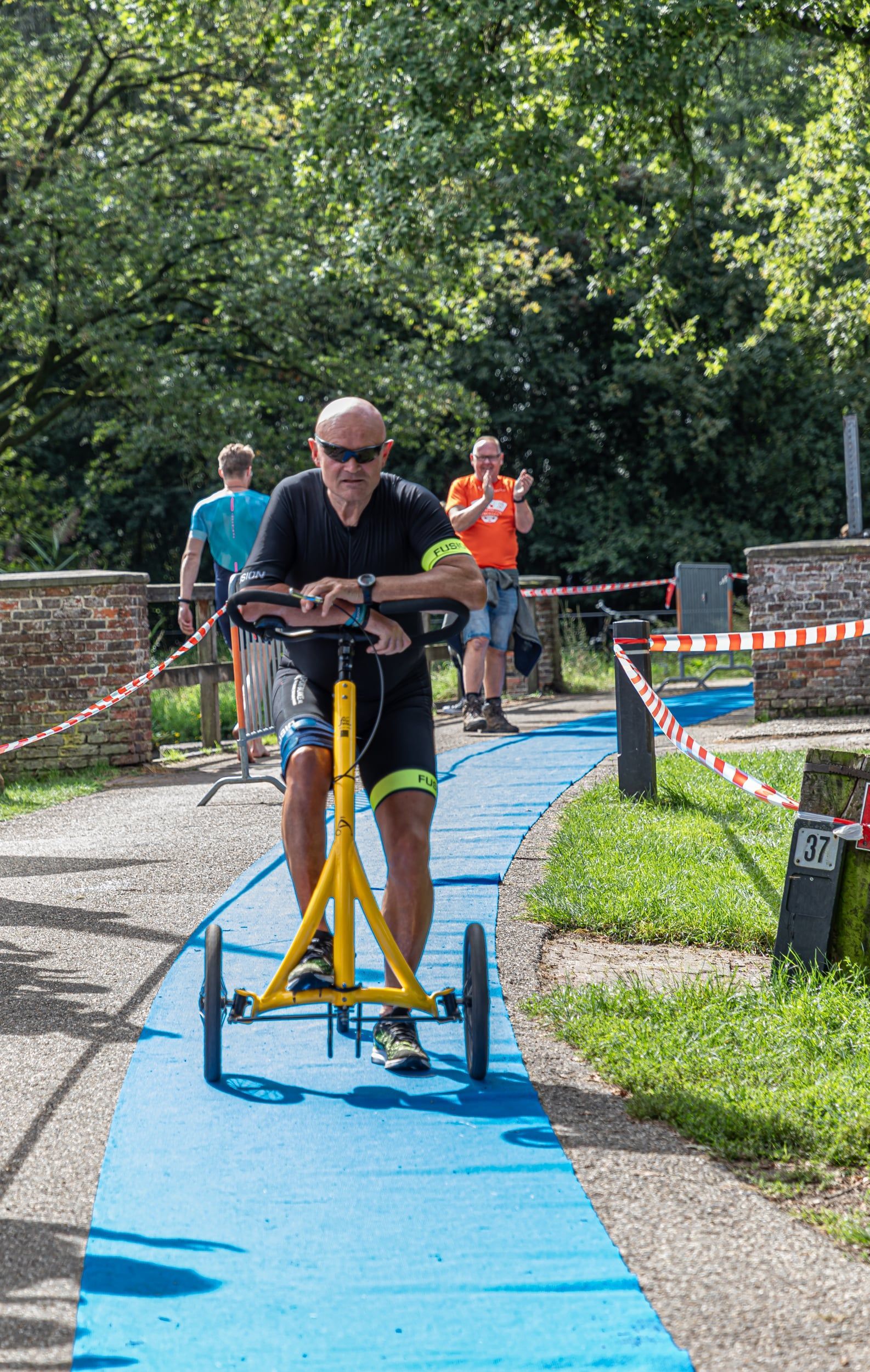Een man rijdt op een gele driewieler op een blauw pad.