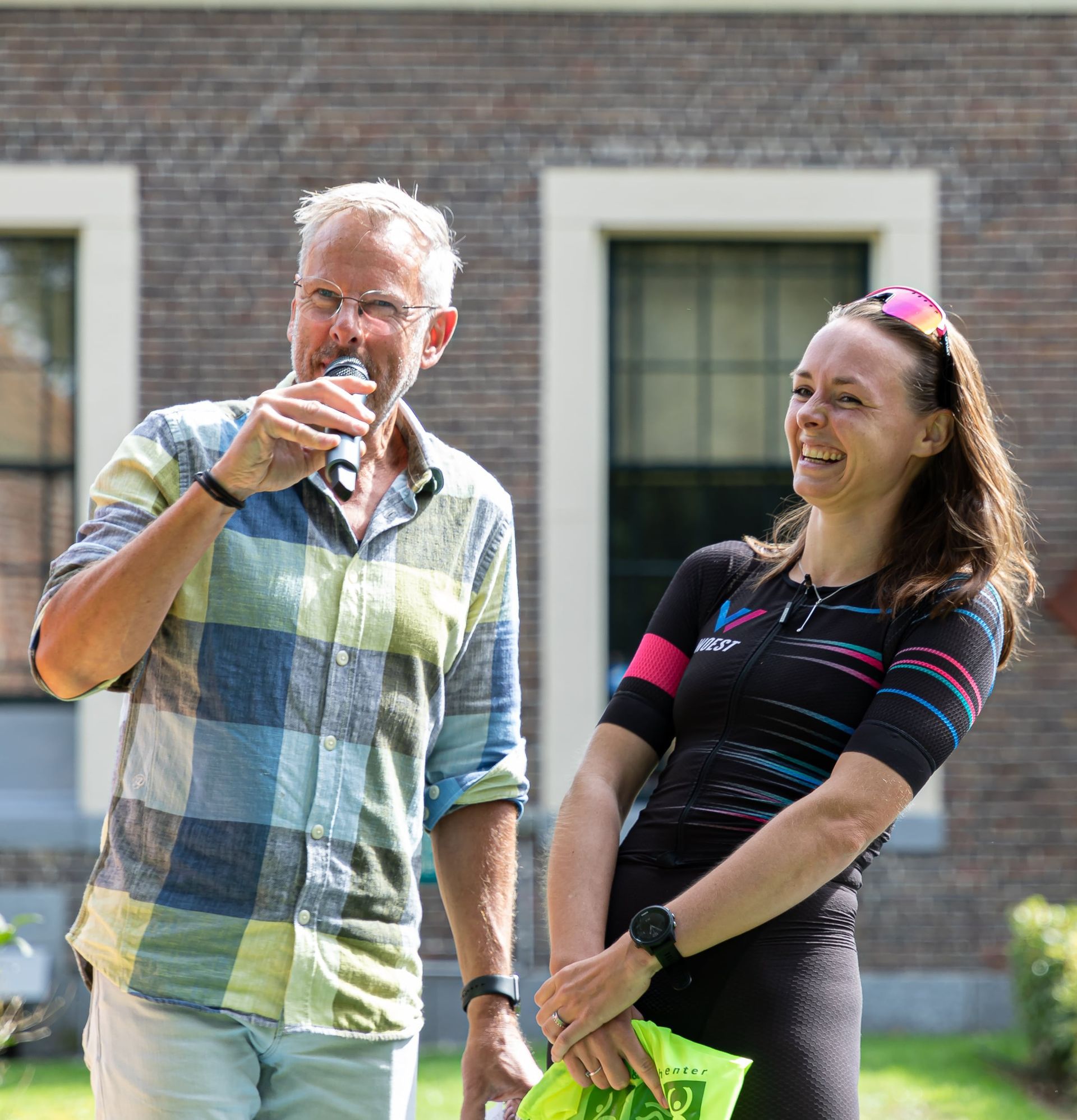Prijsuitreiking Triathlon Eibergen 2023. Een man en een vrouw staan ​​naast elkaar voor een bakstenen gebouw.