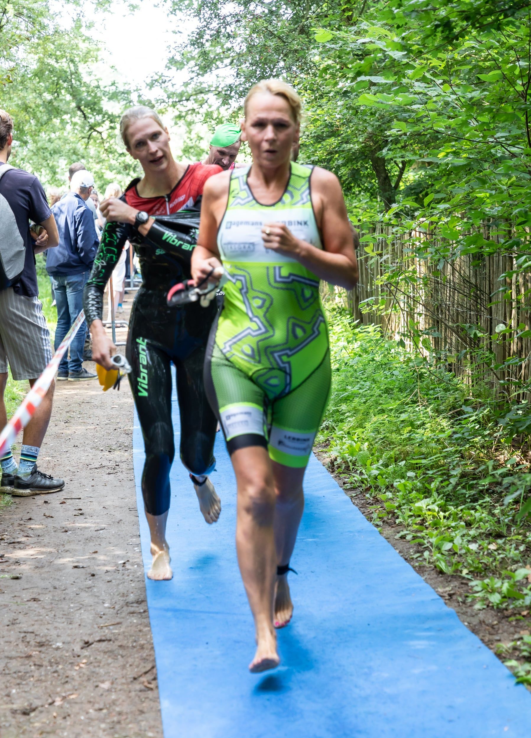 Twee vrouwen rennen op een blauwe mat in het bos.