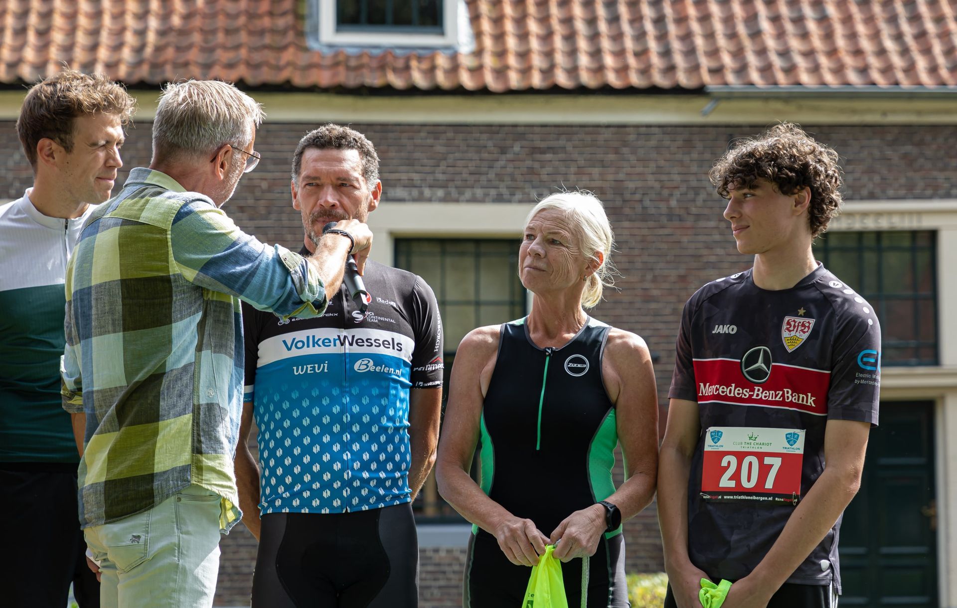 Prijsuitreiking Triathlon Eibergen 2023. Een groep mensen staat voor een bakstenen gebouw.