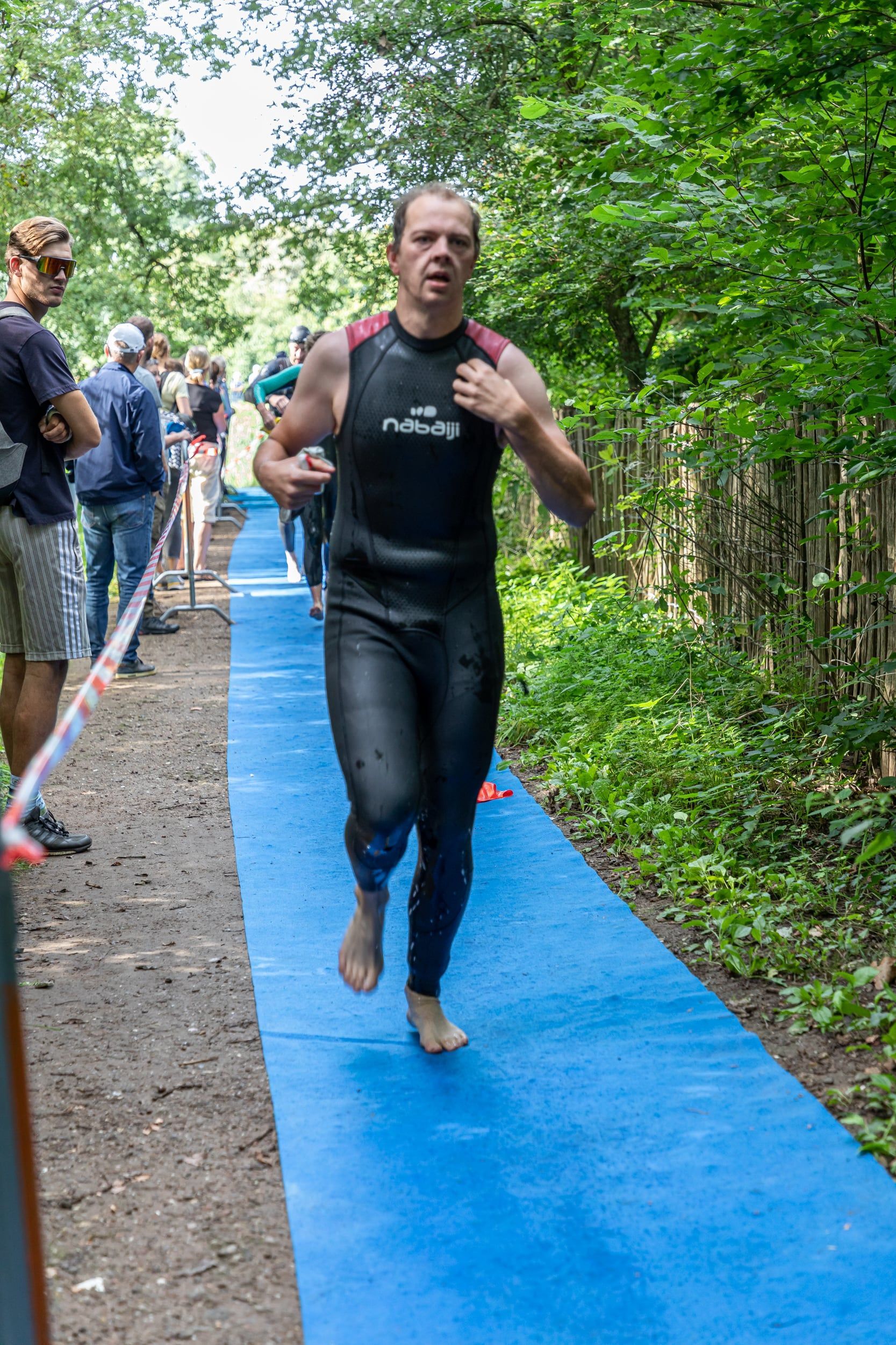 Een man in een wetsuit rent op een blauwe mat in het bos.