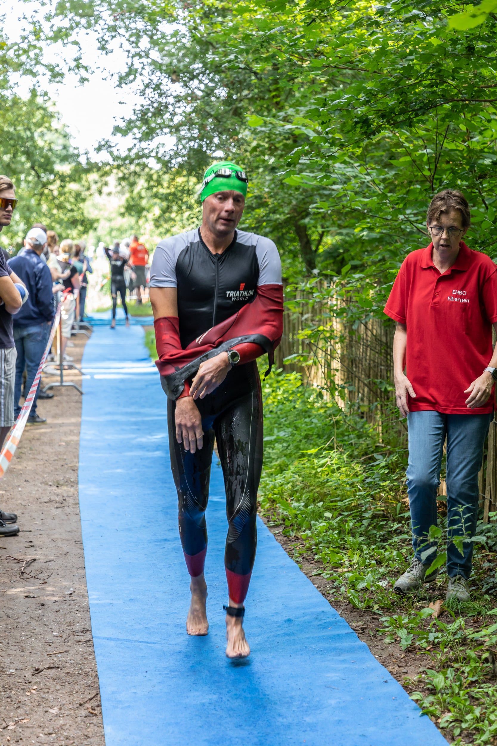 Een man in een wetsuit loopt over een blauw pad.