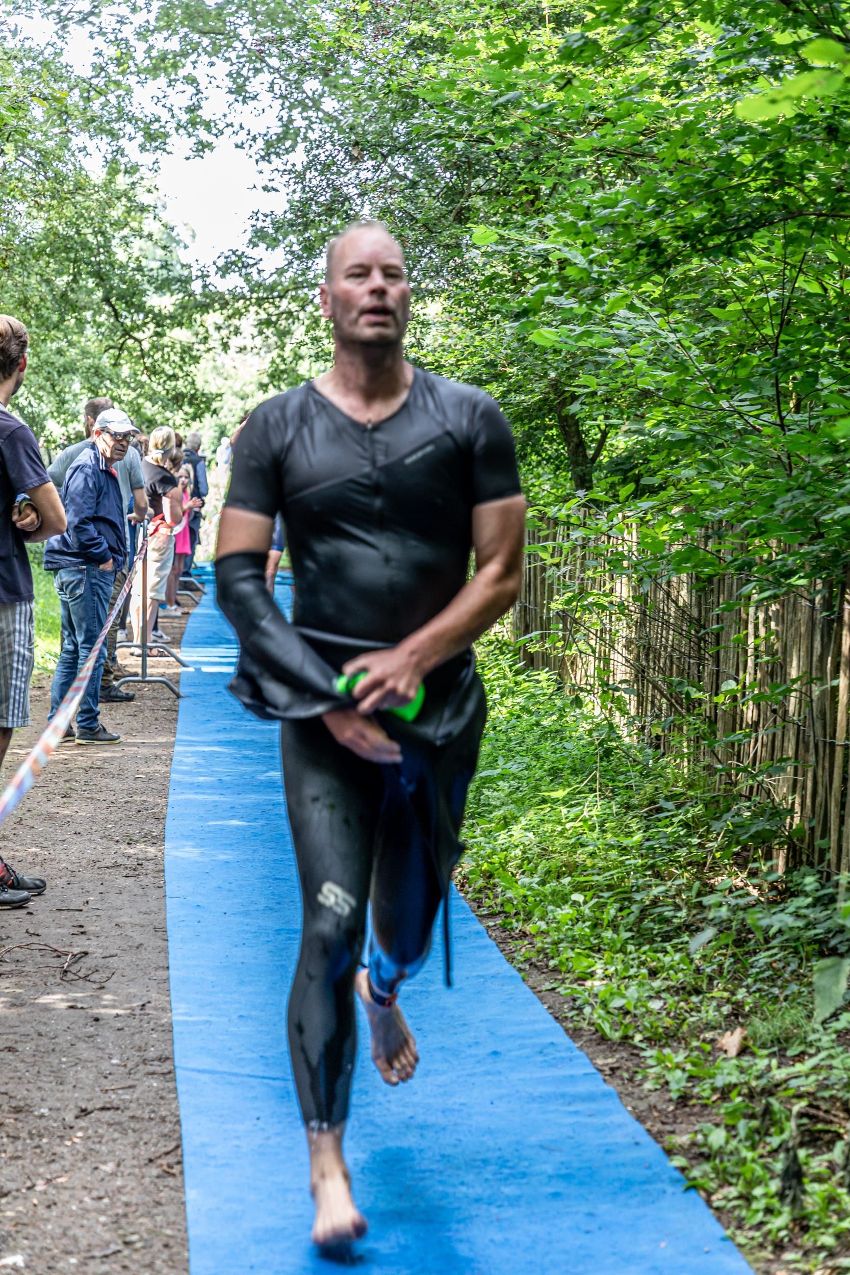 Een man in een wetsuit loopt op een blauwe mat in het bos.